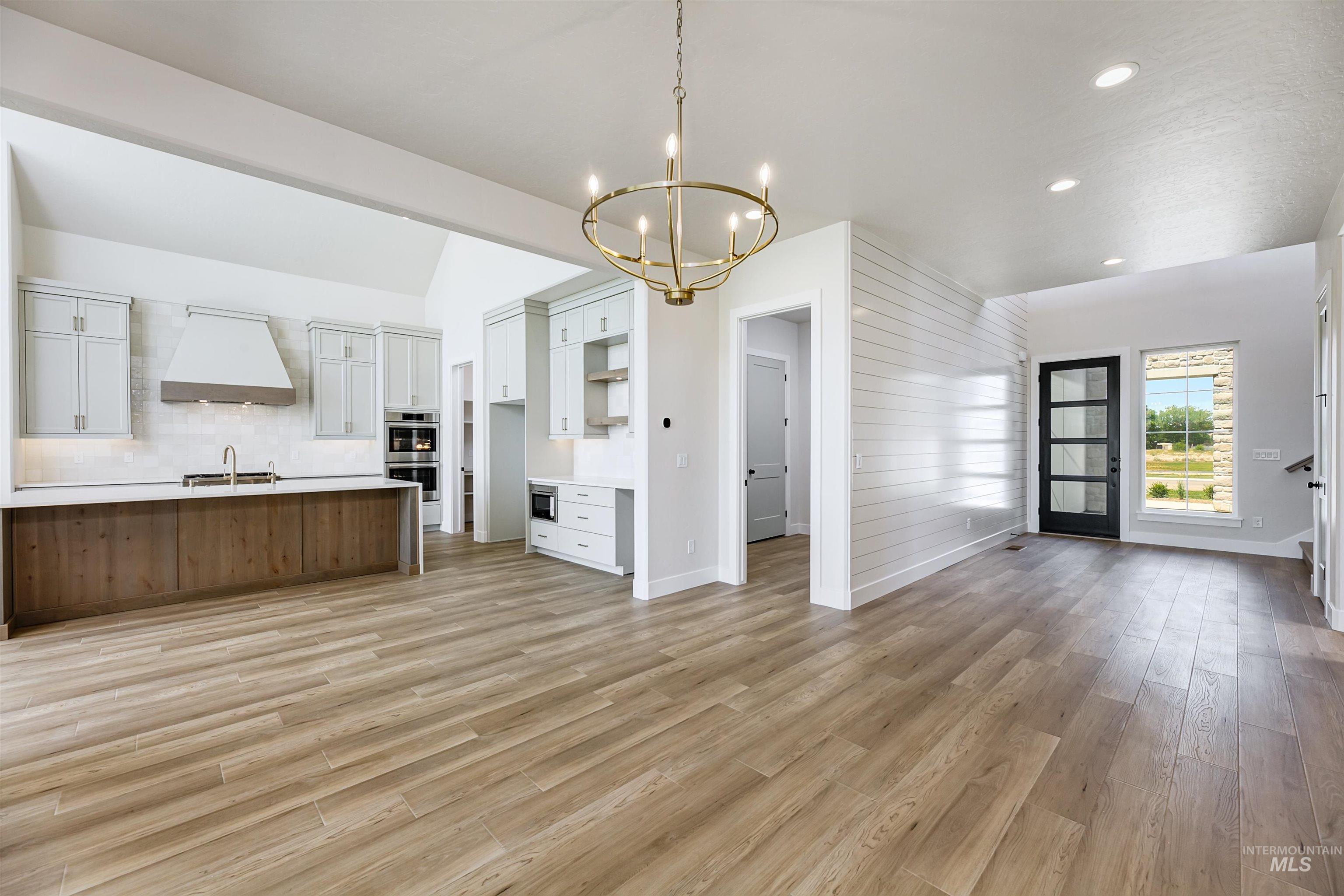 Kitchen featuring open floor plan, hanging light fixtures, custom exhaust hood, light wood-style flooring, and recessed lighting