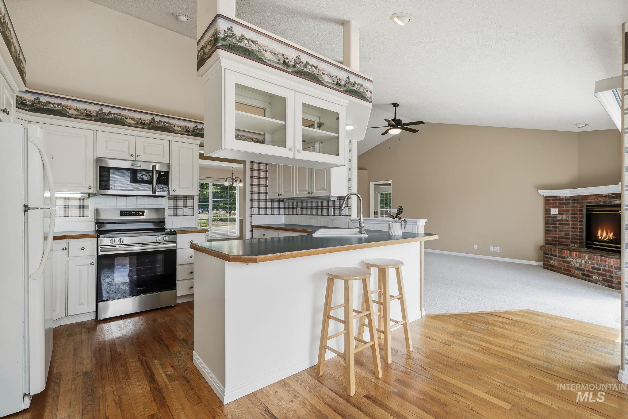 Open concept kitchen featuring an island with sink, white cabinetry, stainless steel appliances, and wood-finish flooring