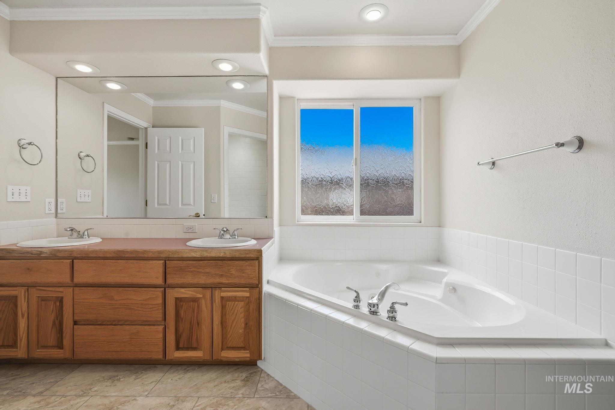 Corner soaking tub with white tile surround and a wood-finish double vanity featuring dual sinks