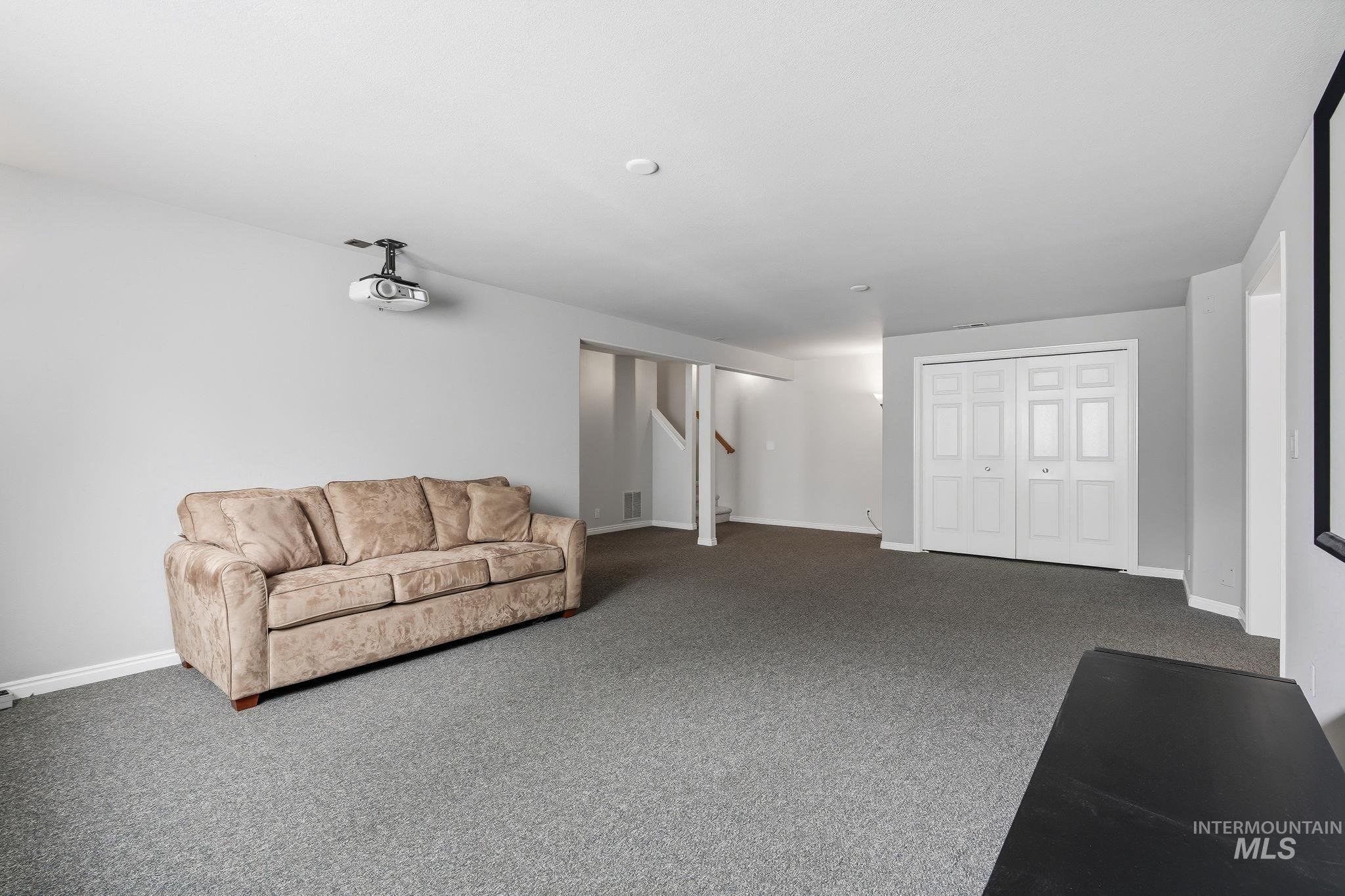 Expansive carpeted room featuring a ceiling-mounted projector, white baseboards, and a built-in closet with bi-fold doors