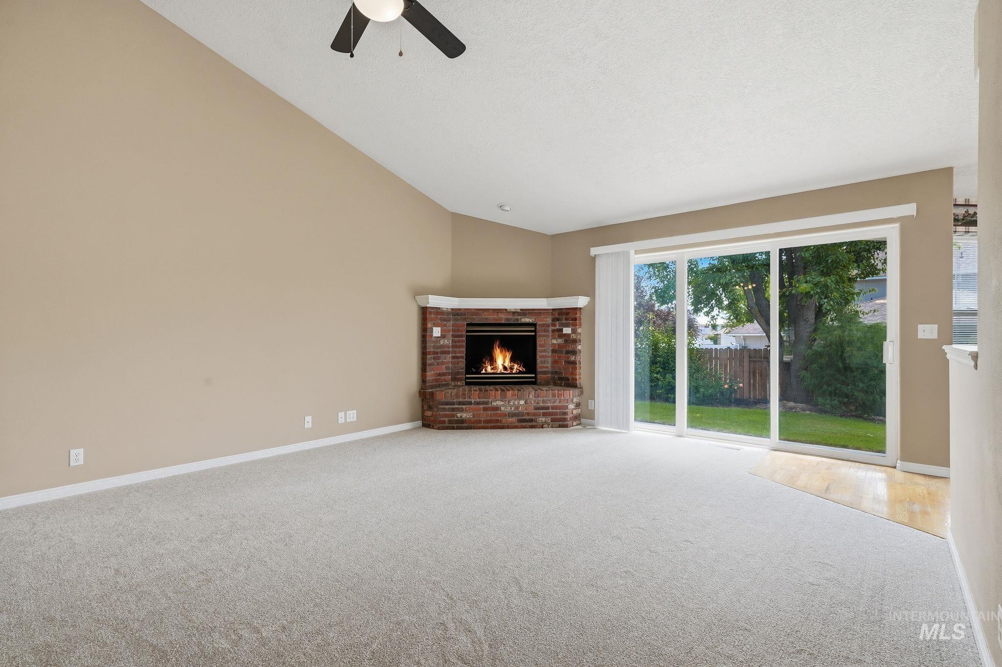 Vaulted ceiling living space featuring a brick fireplace, light-colored carpeting, and a ceiling fan