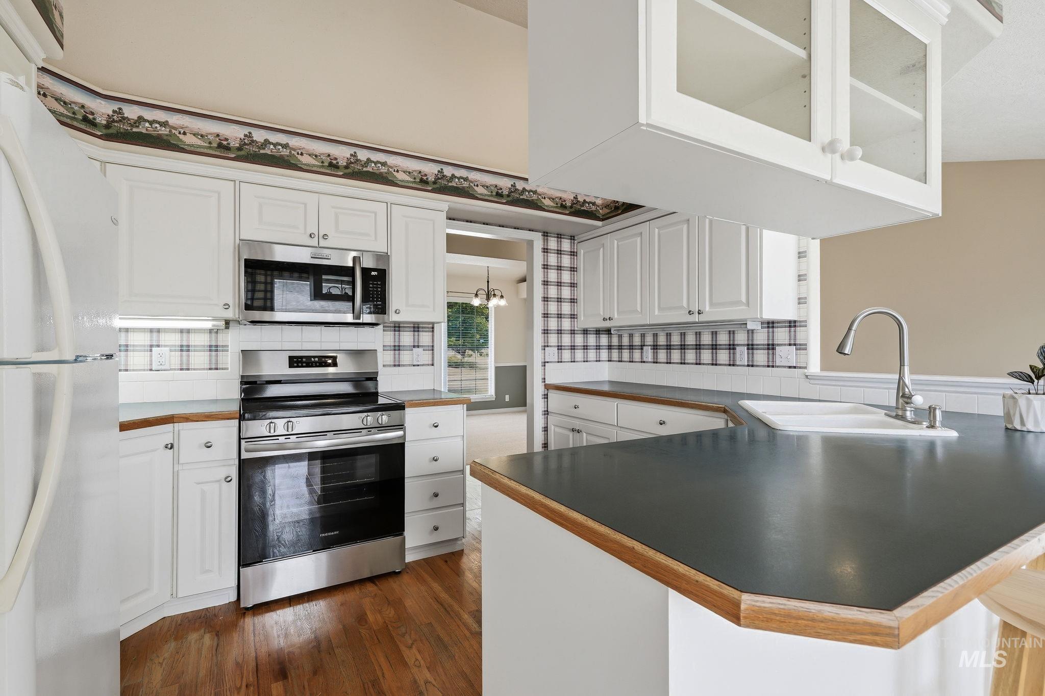 Kitchen featuring white cabinetry, stainless steel appliances, wood-finish flooring, a white porcelain sink, and dark countertops