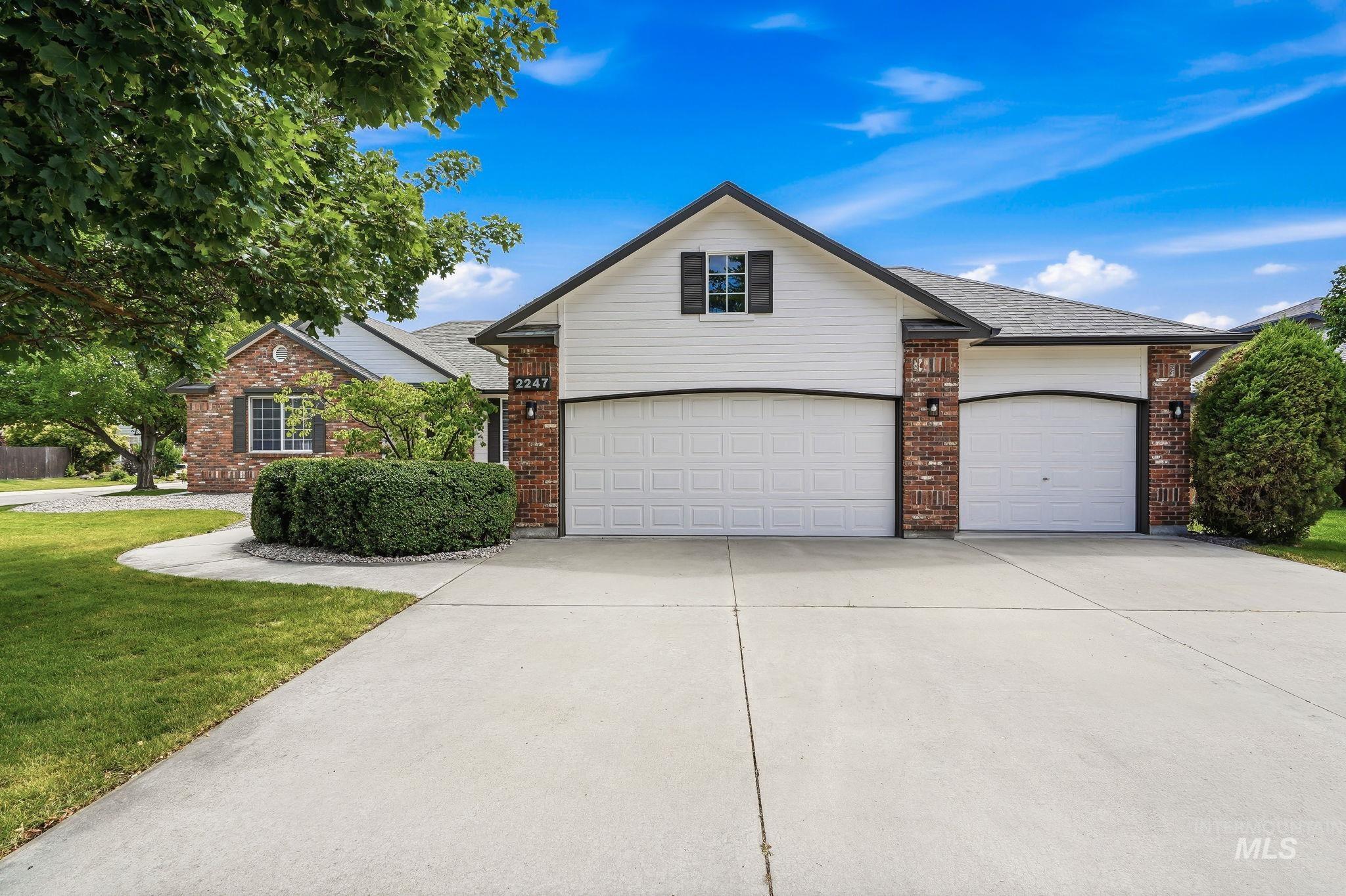 Two-car garage with white paneled doors and dark trim, complemented by brick accents and white siding