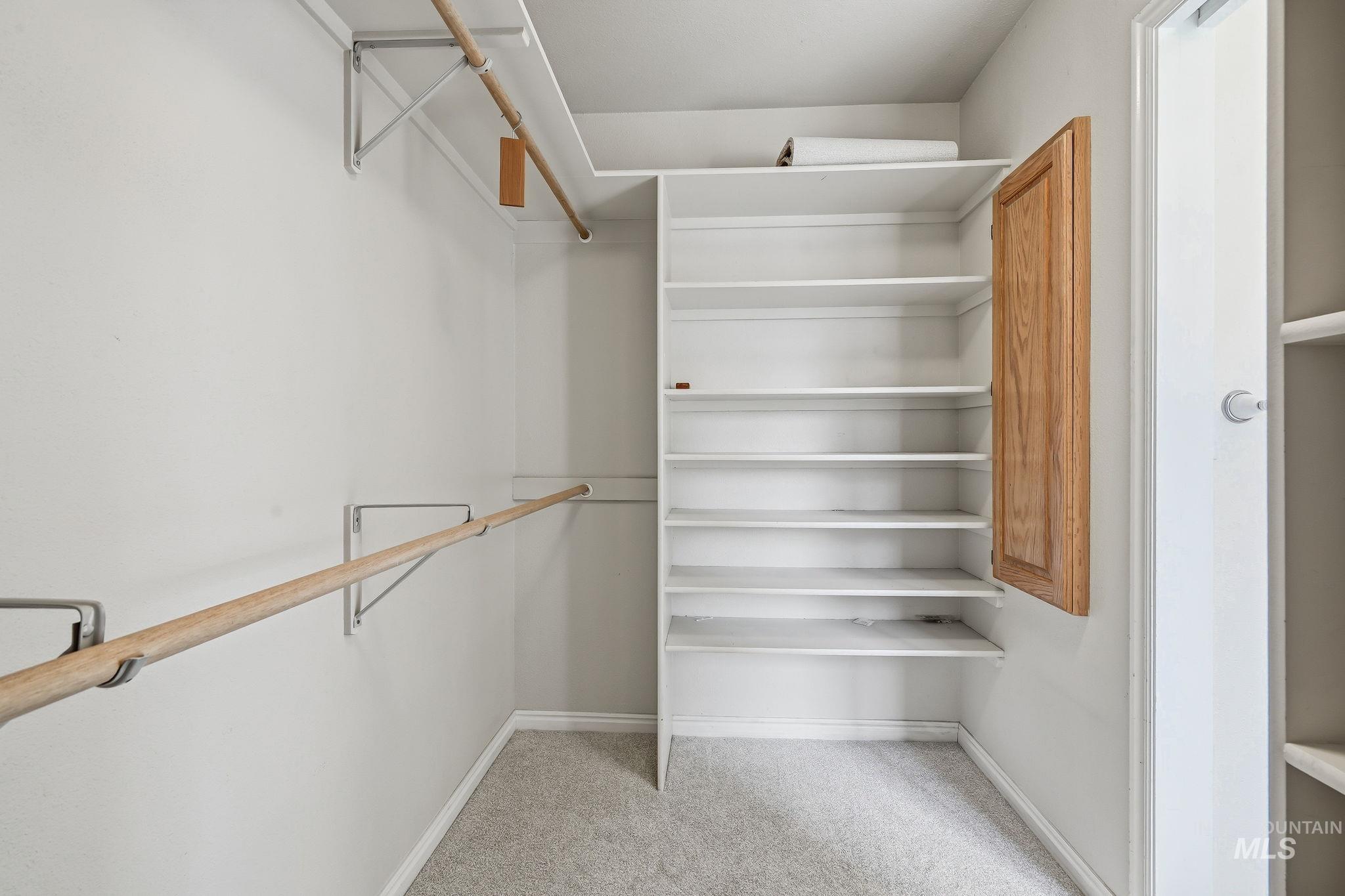 Walk-in closet featuring light gray carpeting, multiple wood hanging rods, built-in white shelving, and a recessed wood cabinet