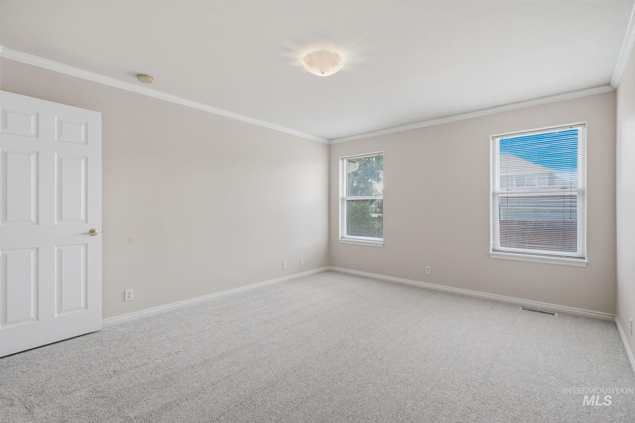 Bright room featuring two windows, crown molding, light-toned carpeting, and a flush mount ceiling light