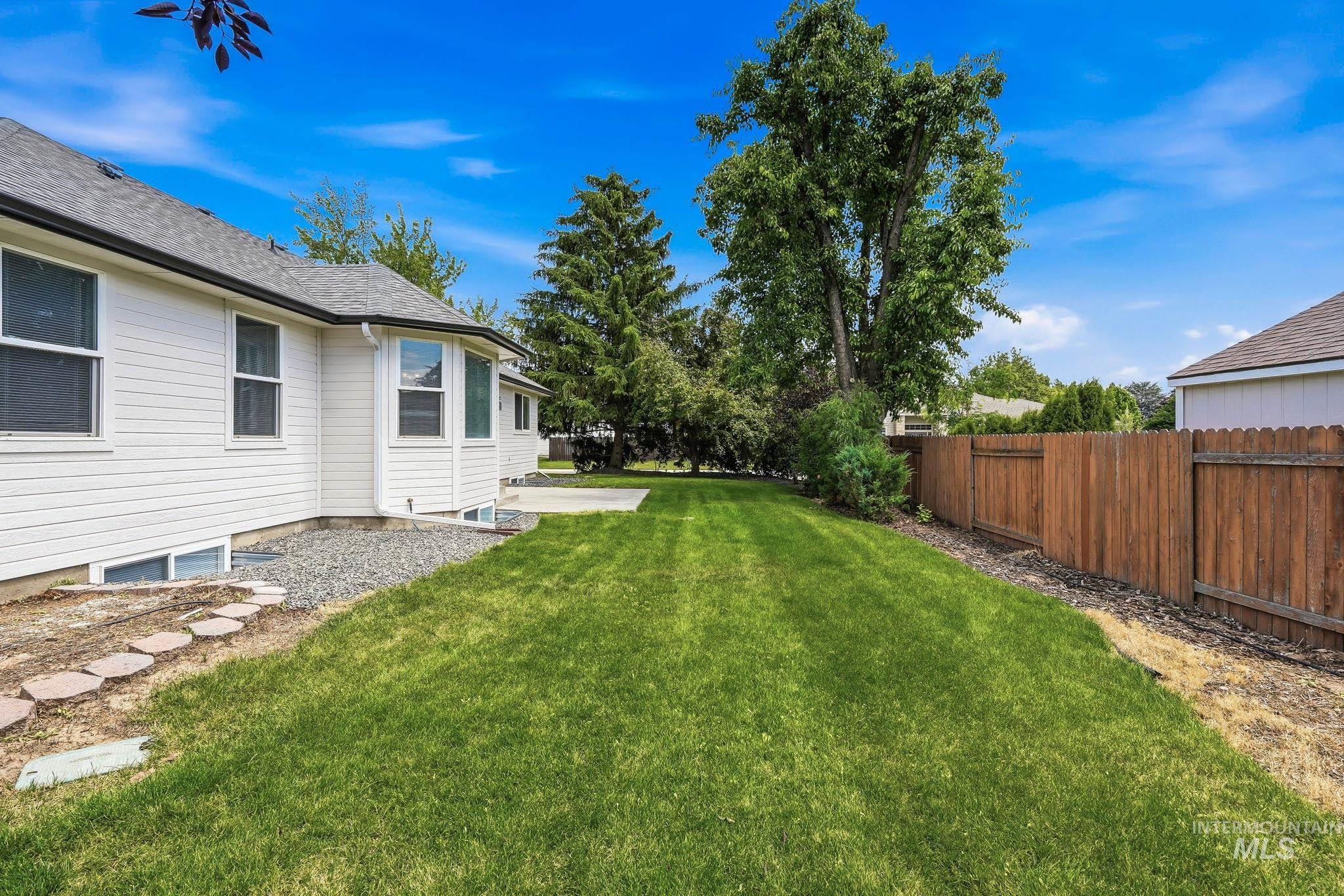 Expansive fenced backyard featuring a verdant lawn, mature trees, and a concrete patio