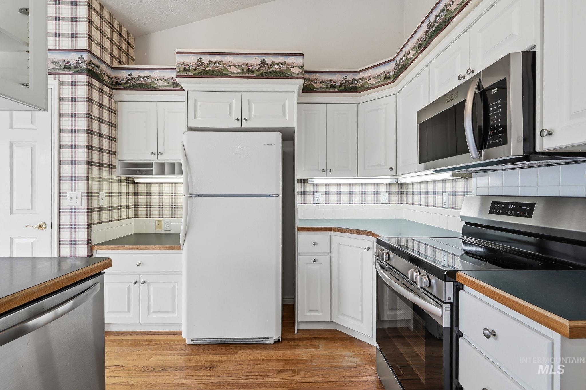 Kitchen featuring white cabinetry, wood-finish flooring, stainless steel appliances, and a vaulted ceiling