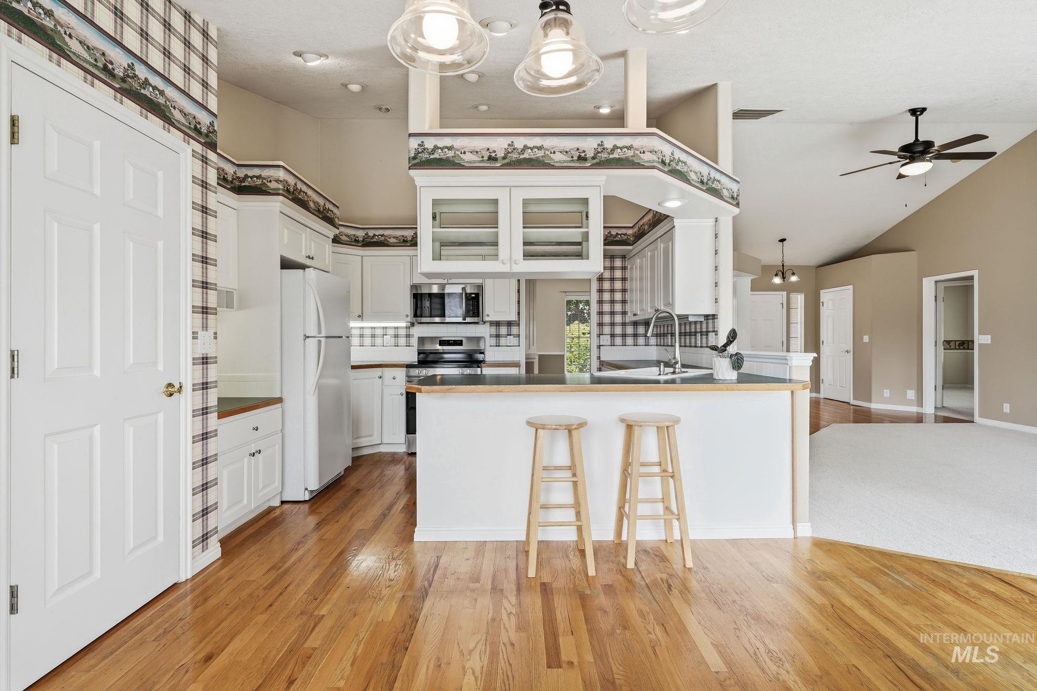 Kitchen featuring wood-finish flooring, white cabinetry, integrated appliances, and a breakfast bar