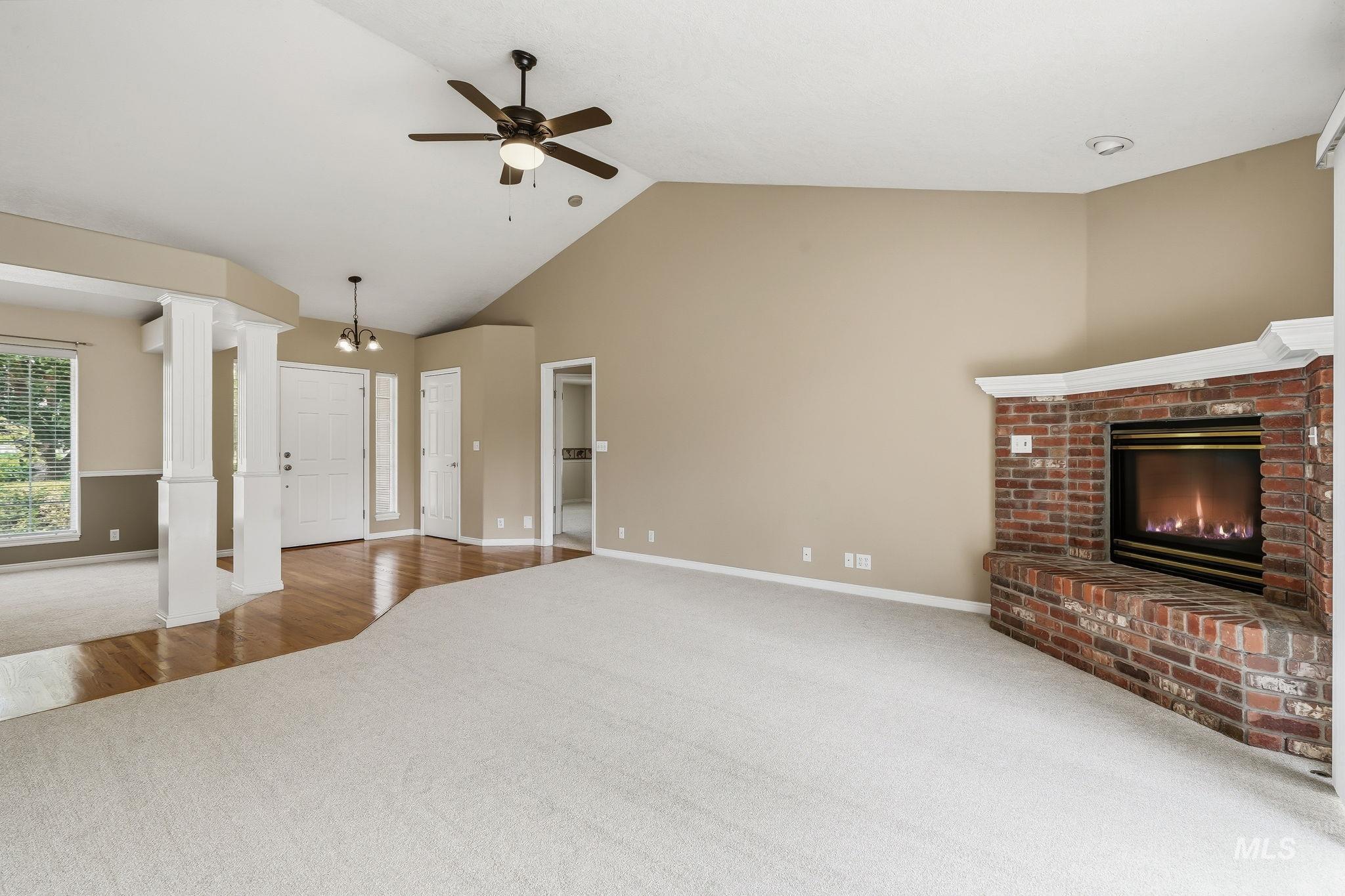 Vaulted ceilings with a ceiling fan, a brick-surround fireplace with a white mantel, and light carpeting throughout