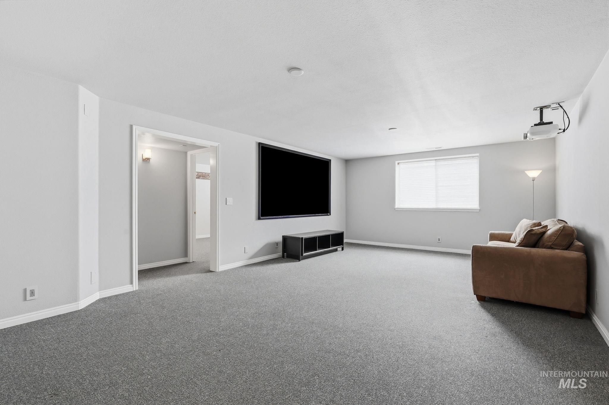 Spacious room featuring light gray walls, gray carpeting, a large wall-mounted screen, and a ceiling-mounted projector