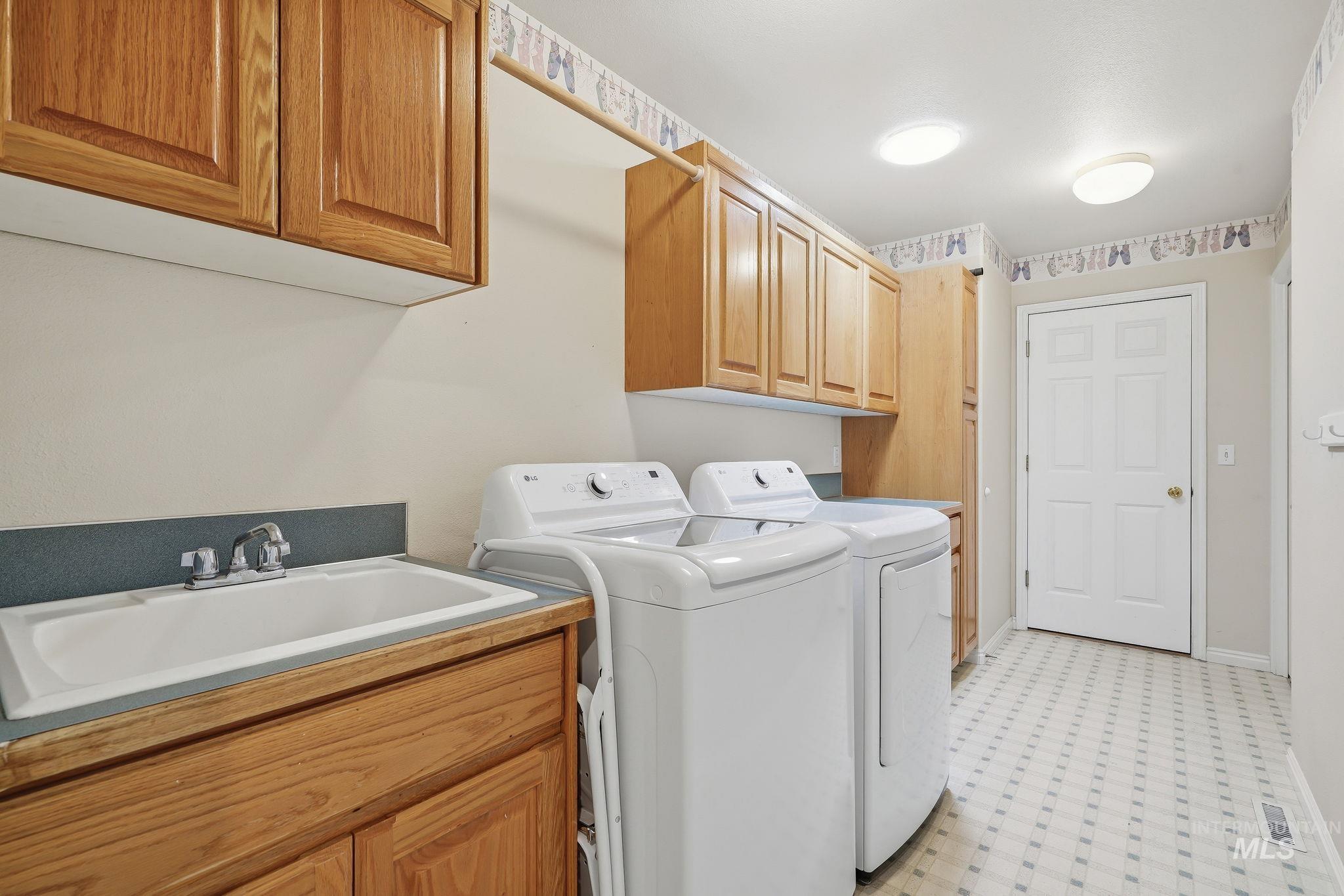 Laundry room featuring a utility sink, light wood cabinetry, and patterned floor tile