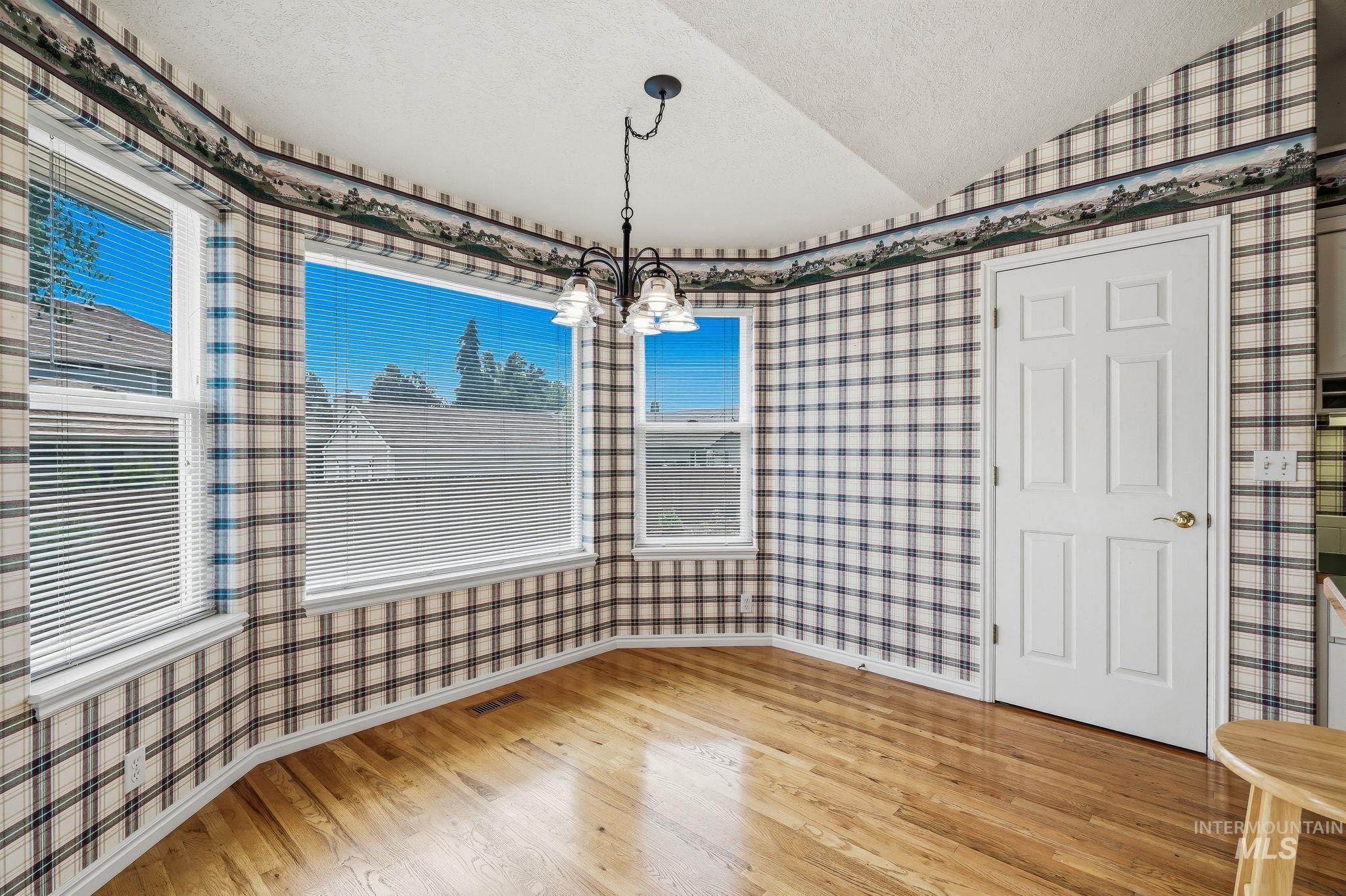 Bay window area featuring wood-finish flooring, multiple windows with blinds, a white paneled door, and an overhead chandelier with decorative shades