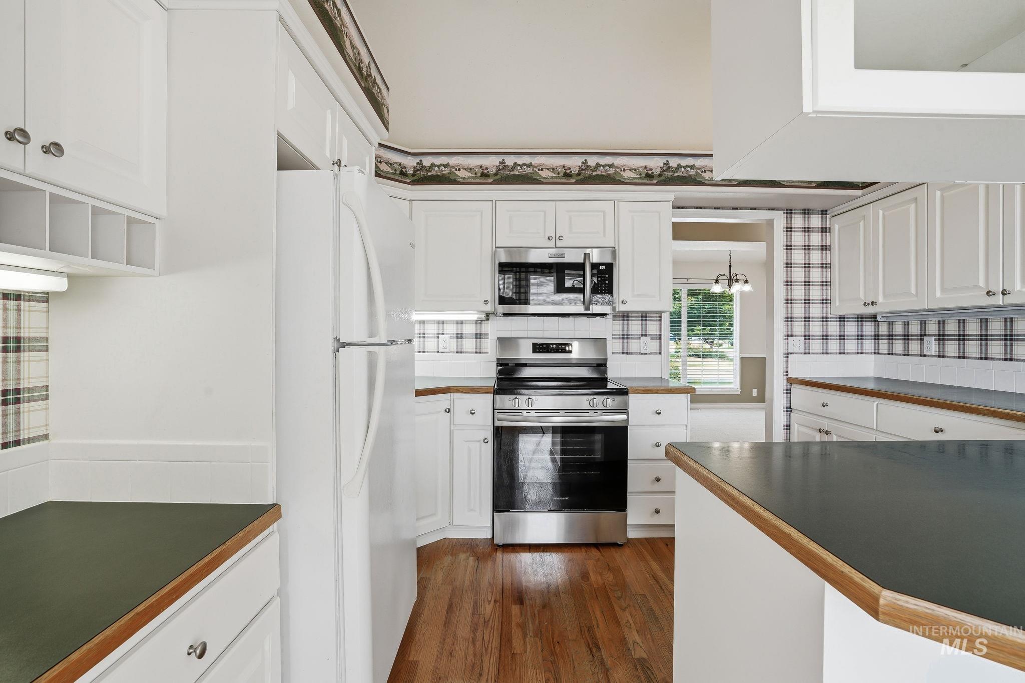 Kitchen featuring white cabinetry, dark countertops with wood trim, wood-finish flooring, and stainless steel appliances including an oven, microwave, and refrigerator