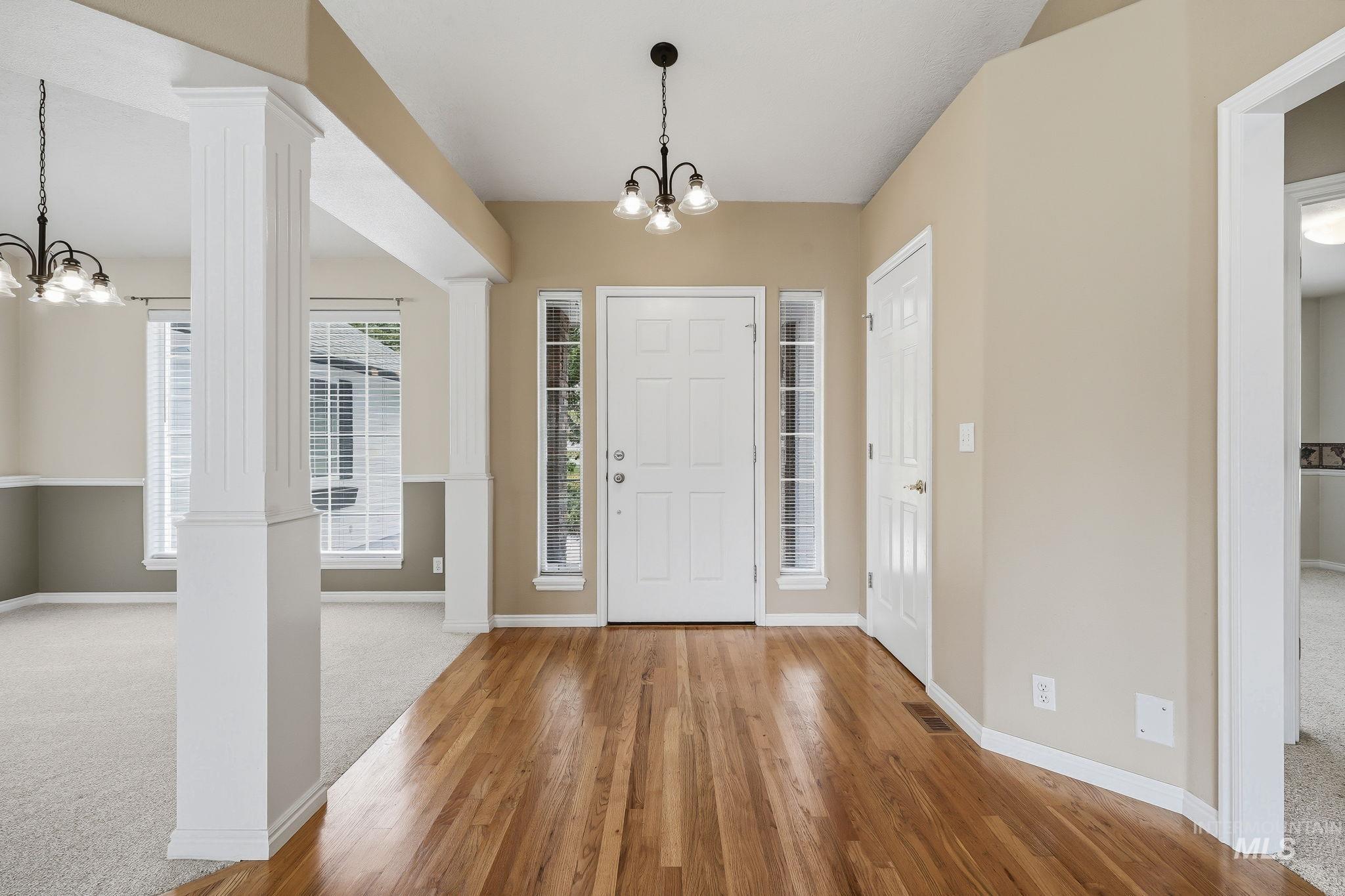 Foyer featuring wood-finish flooring, a white paneled entry door with sidelights, and a vaulted ceiling