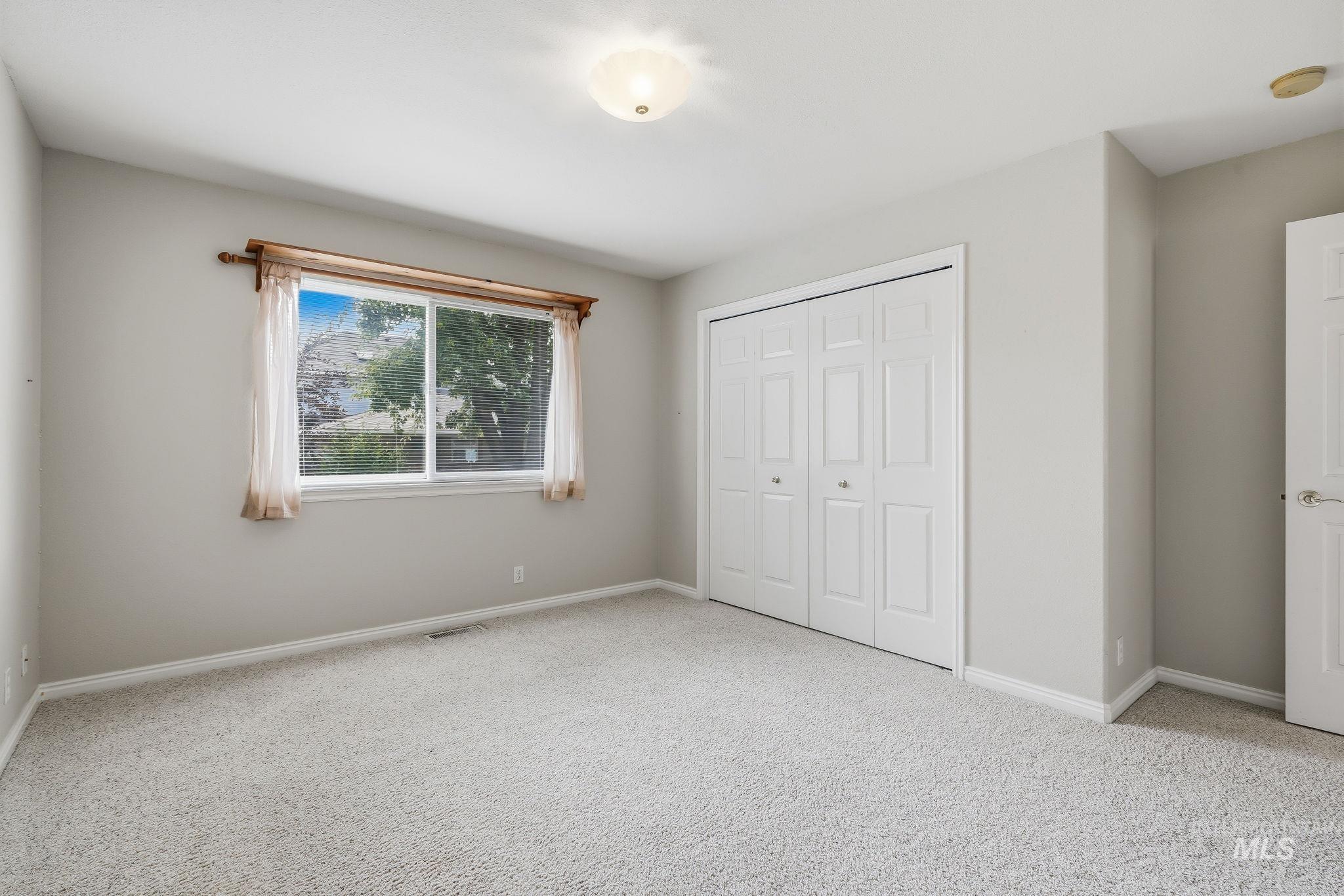 Carpeted room with a double-pane window, white trim, white bi-fold closet doors, and an overhead flush-mount light fixture