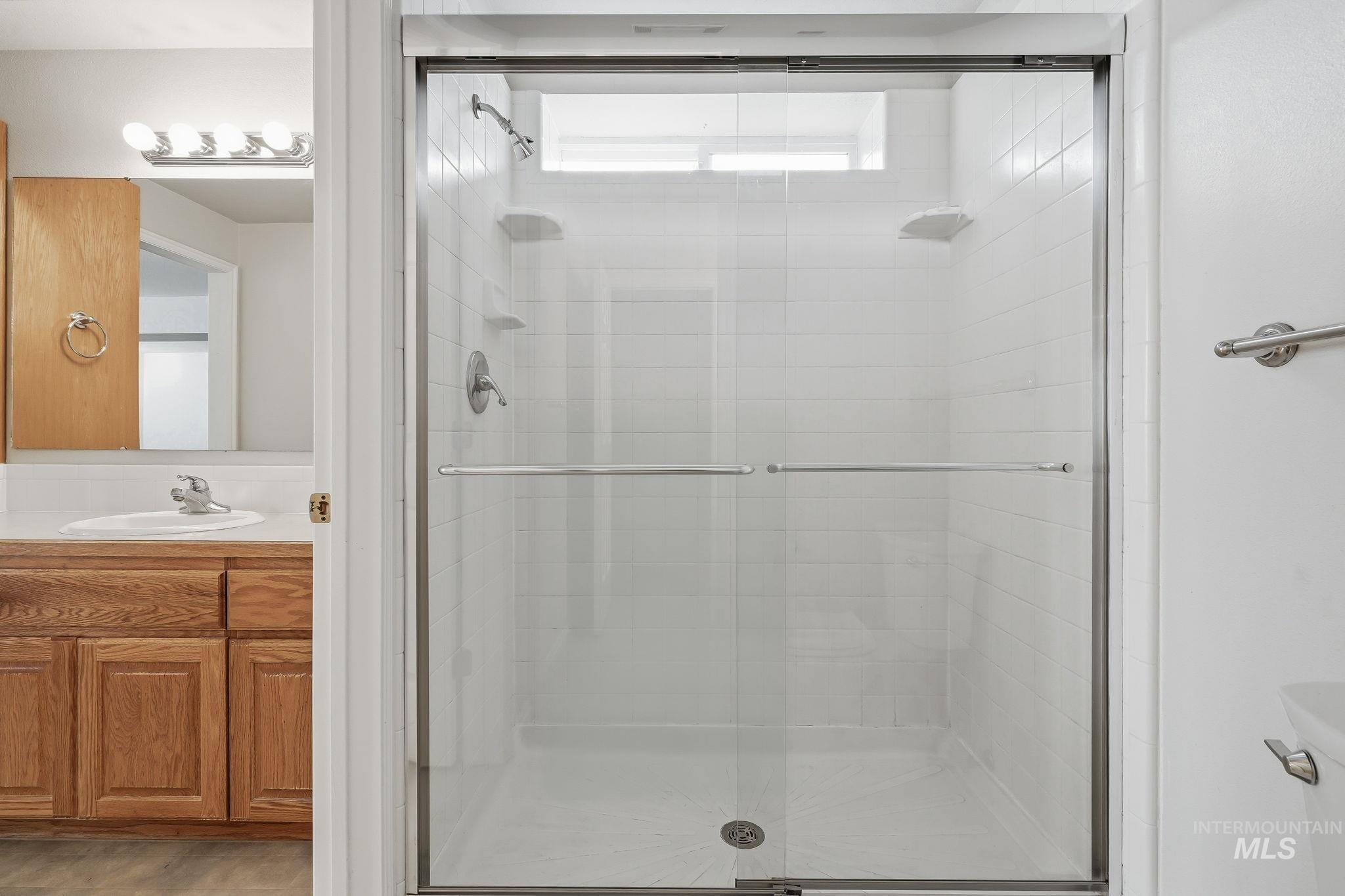 Shower enclosure with sliding glass doors, white tiled walls, and a built-in shelf, complemented by a wood-finish vanity with an integrated sink and mirror