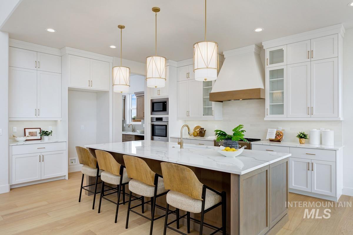 Kitchen featuring pendant lighting, custom exhaust hood, white cabinetry, a breakfast bar, and light stone countertops