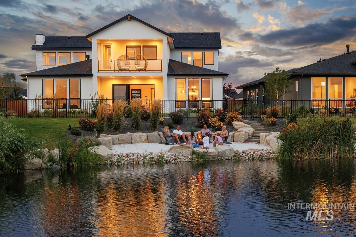 Back of property at dusk featuring a balcony, a patio area, roof with shingles, a water view, and stucco siding