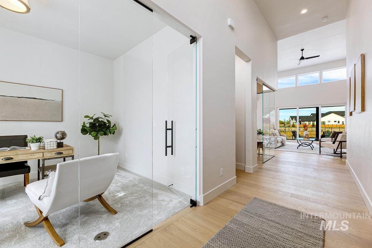 Office space featuring a ceiling fan, light wood-type flooring, and a towering ceiling