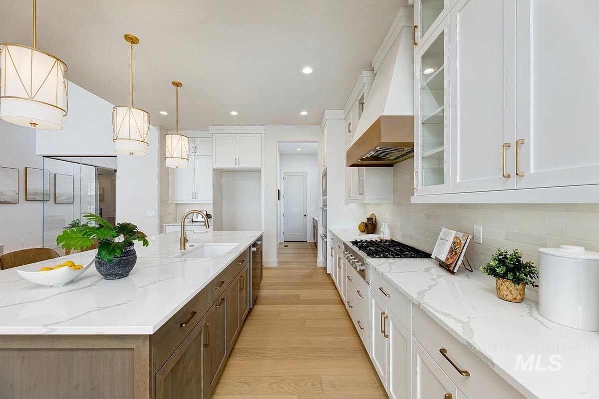 Kitchen featuring glass insert cabinets, light stone counters, hanging light fixtures, white cabinets, and recessed lighting
