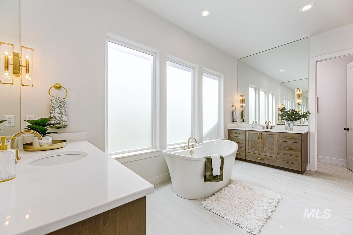 Full bathroom featuring two vanities, a freestanding tub, recessed lighting, and a chandelier