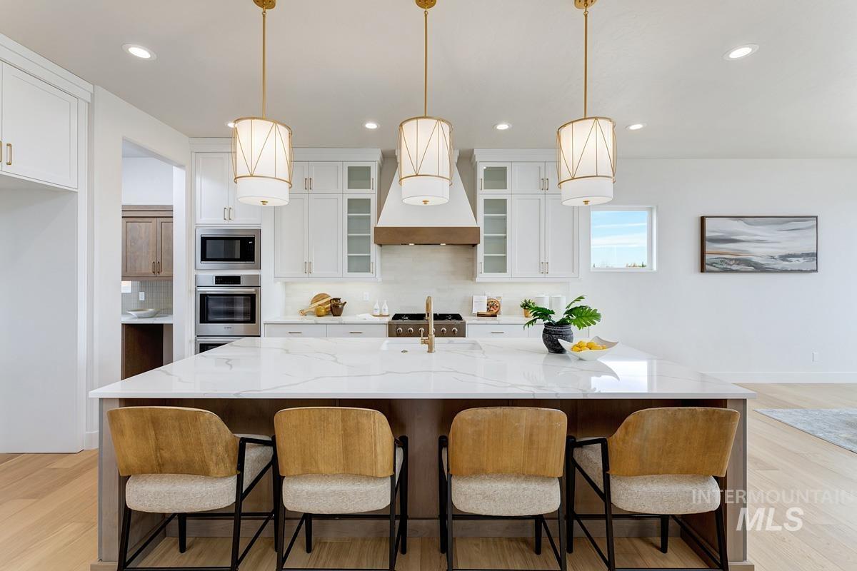 Kitchen with light wood-style flooring, white cabinetry, custom exhaust hood, glass insert cabinets, and recessed lighting