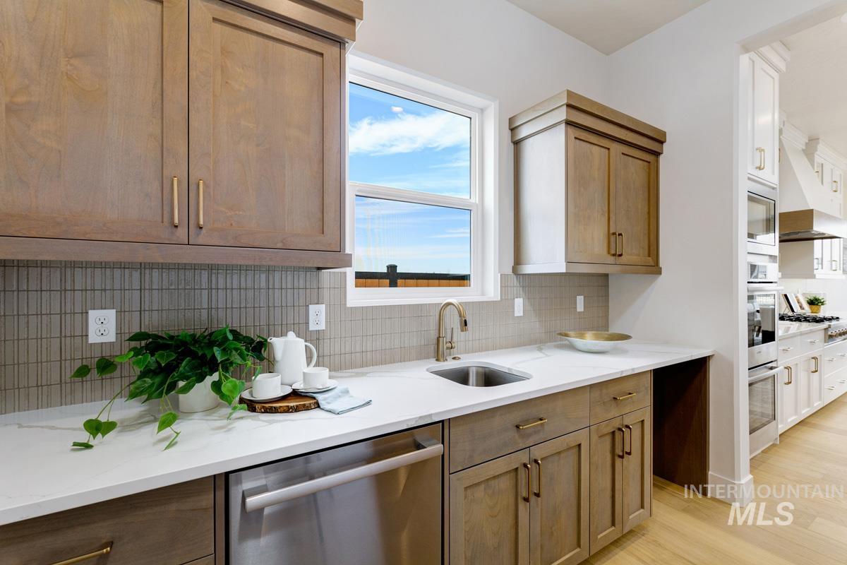Kitchen featuring appliances with stainless steel finishes, decorative backsplash, extractor fan, light stone countertops, and light wood-style floors