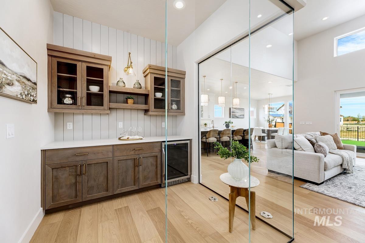 Bar with glass insert cabinets, open shelves, beverage cooler, pendant lighting, and light wood-style flooring