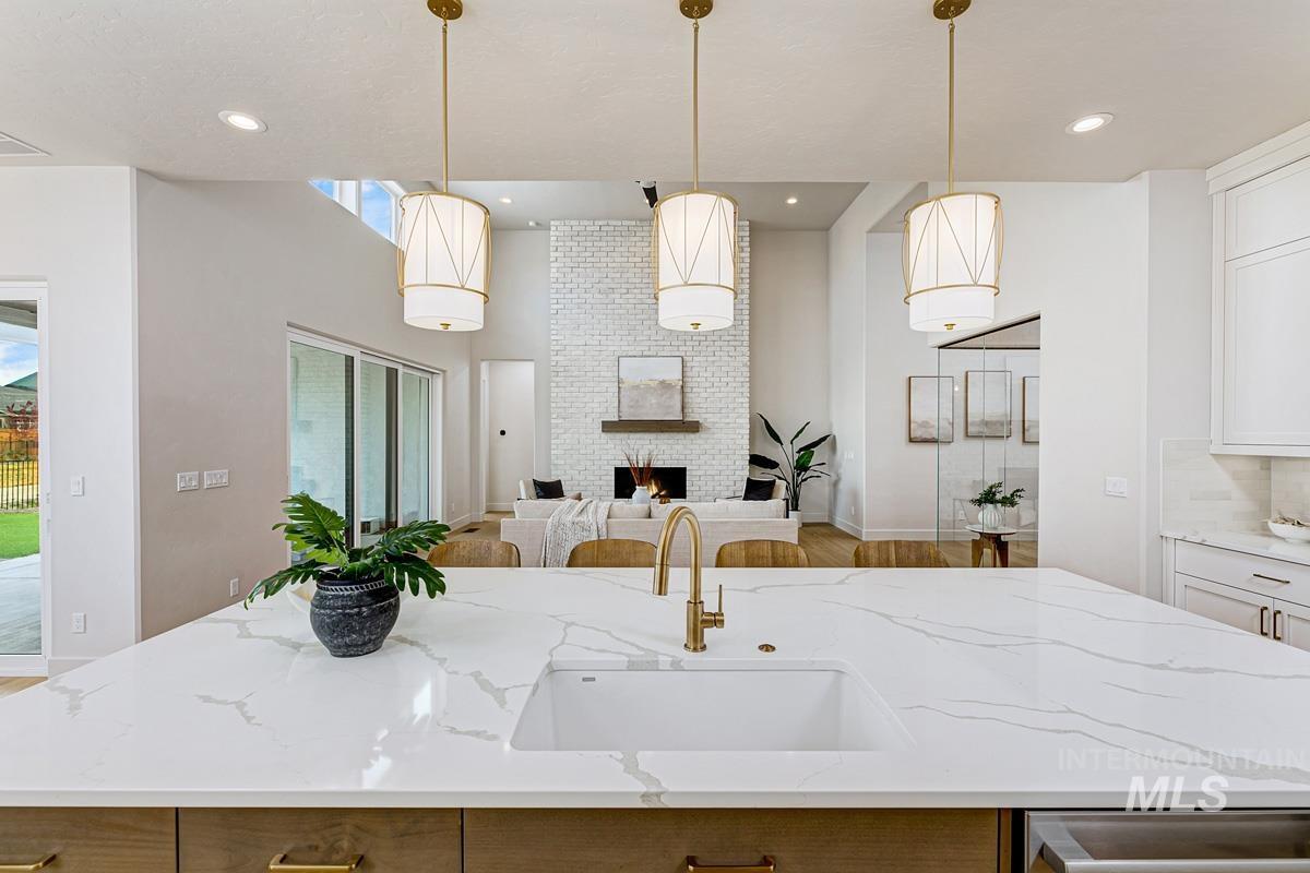 Kitchen with an island with sink, light stone countertops, hanging light fixtures, open floor plan, and a brick fireplace