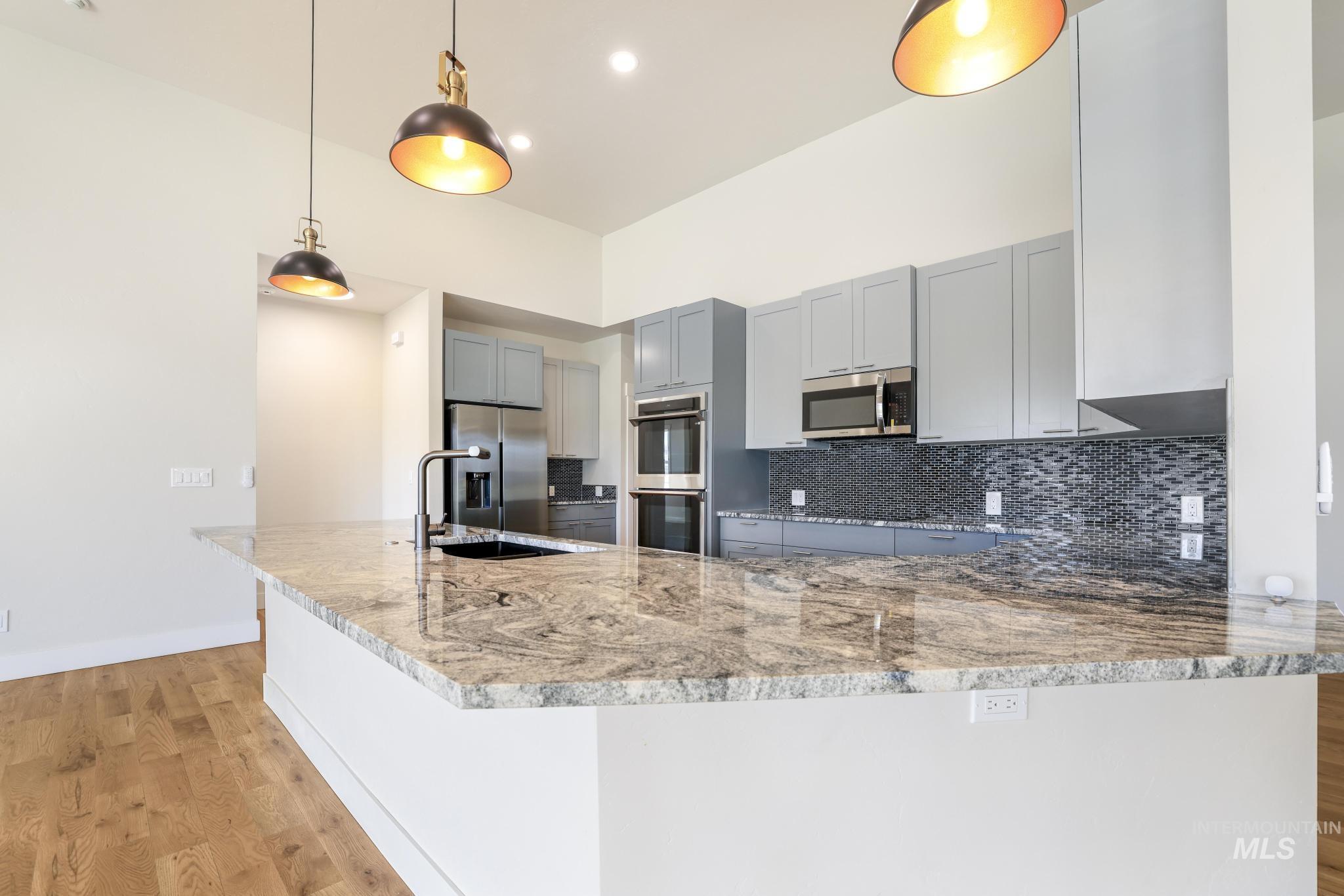 Kitchen with gray cabinets, light wood-style flooring, a peninsula, decorative light fixtures, and light stone counters