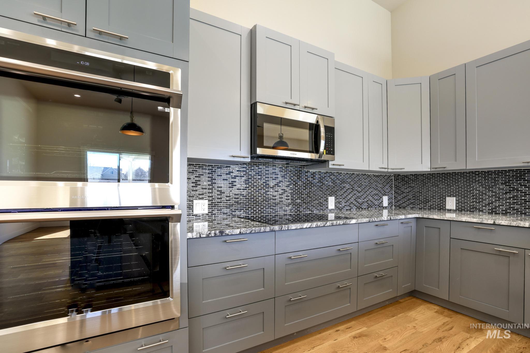 Kitchen featuring stainless steel appliances, light stone countertops, light wood-style flooring, two tone cabinets, and decorative backsplash