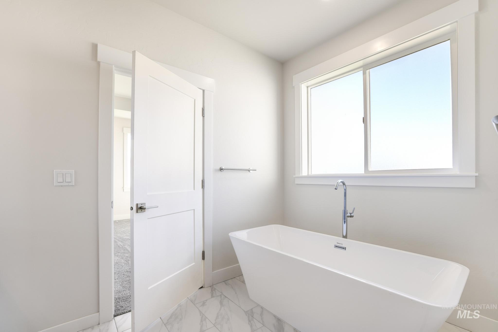 Bathroom featuring a soaking tub and light marble finish flooring