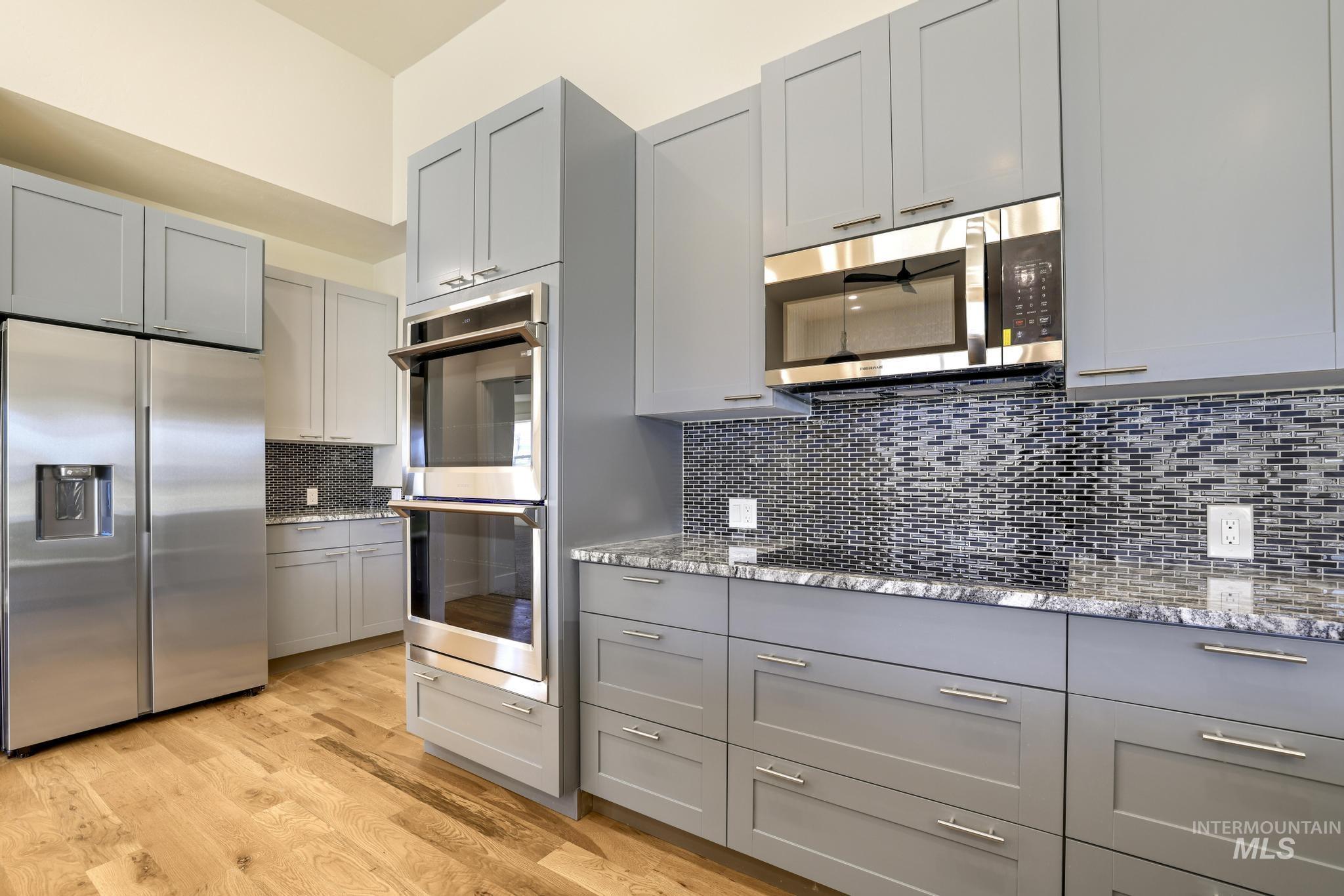 Kitchen featuring gray cabinets, stainless steel appliances, light stone countertops, backsplash, and light wood-type flooring