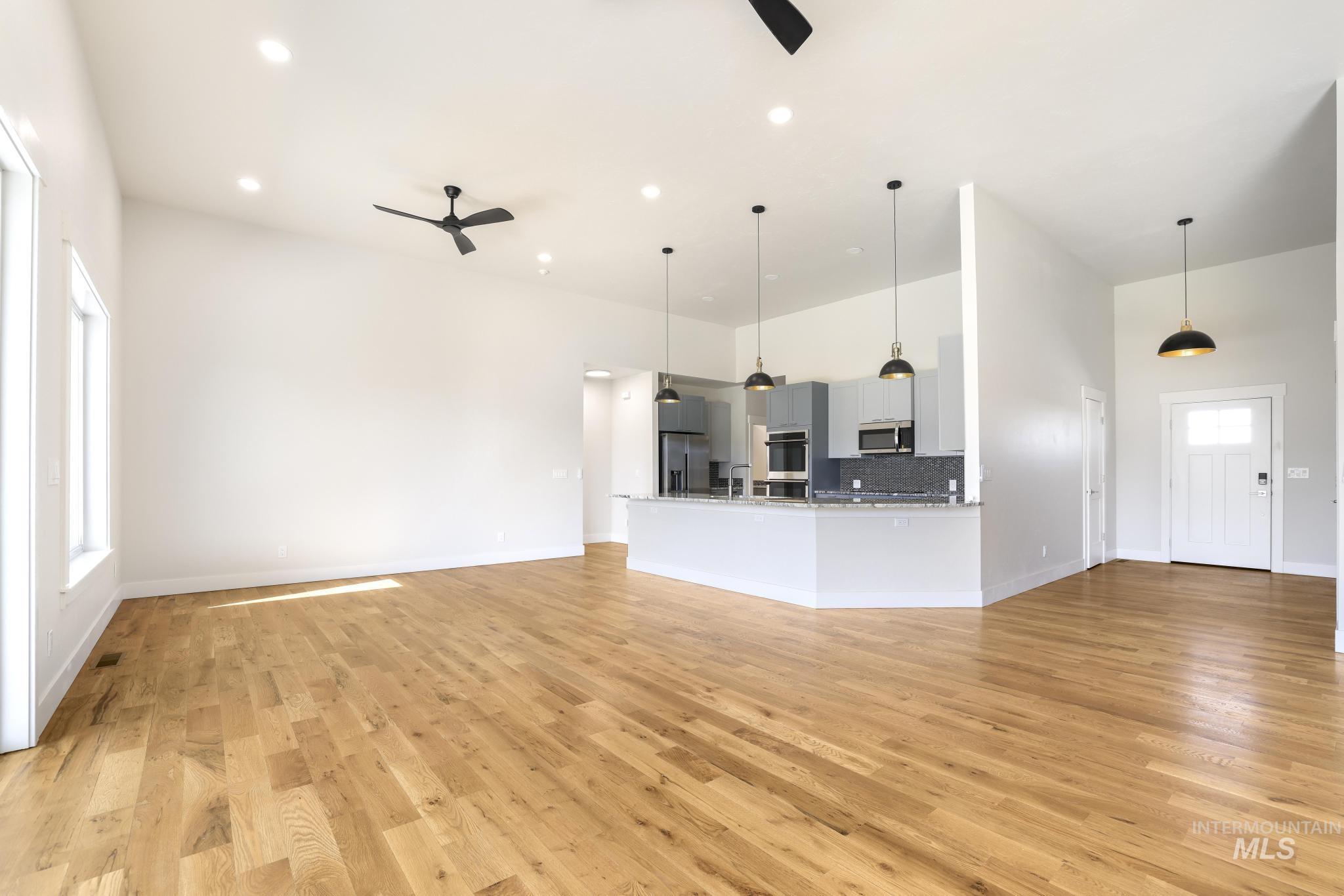 Unfurnished living room featuring a high ceiling, light wood-type flooring, a ceiling fan, and recessed lighting