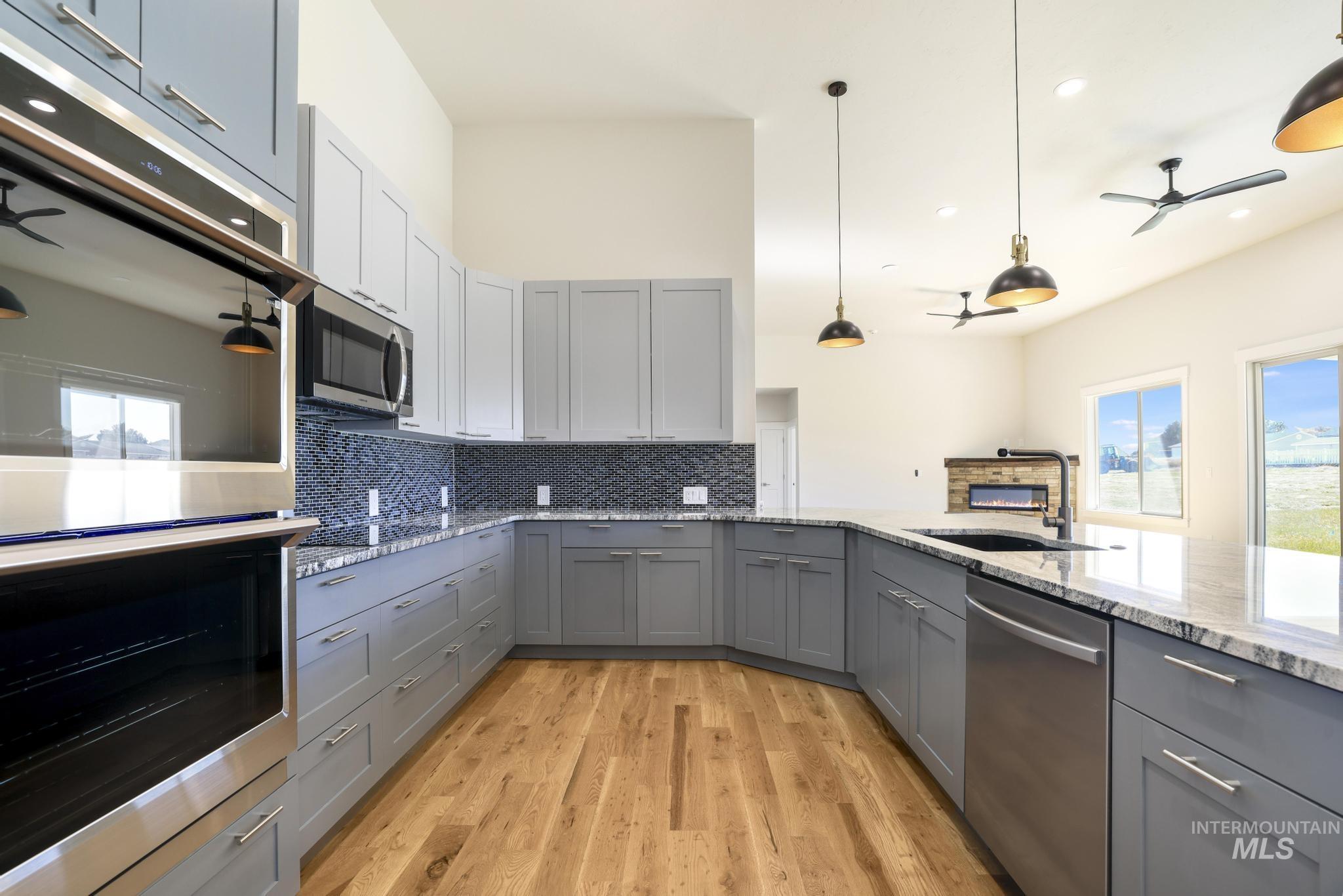 Kitchen featuring ceiling fan, gray cabinetry, stainless steel appliances, light stone counters, and tasteful backsplash