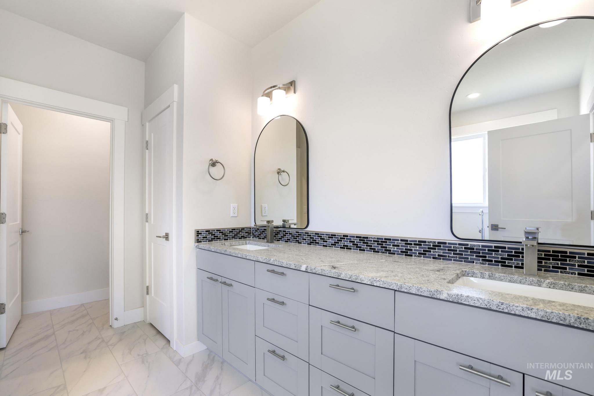 Full bath featuring double vanity, light marble finish floors, and tasteful backsplash