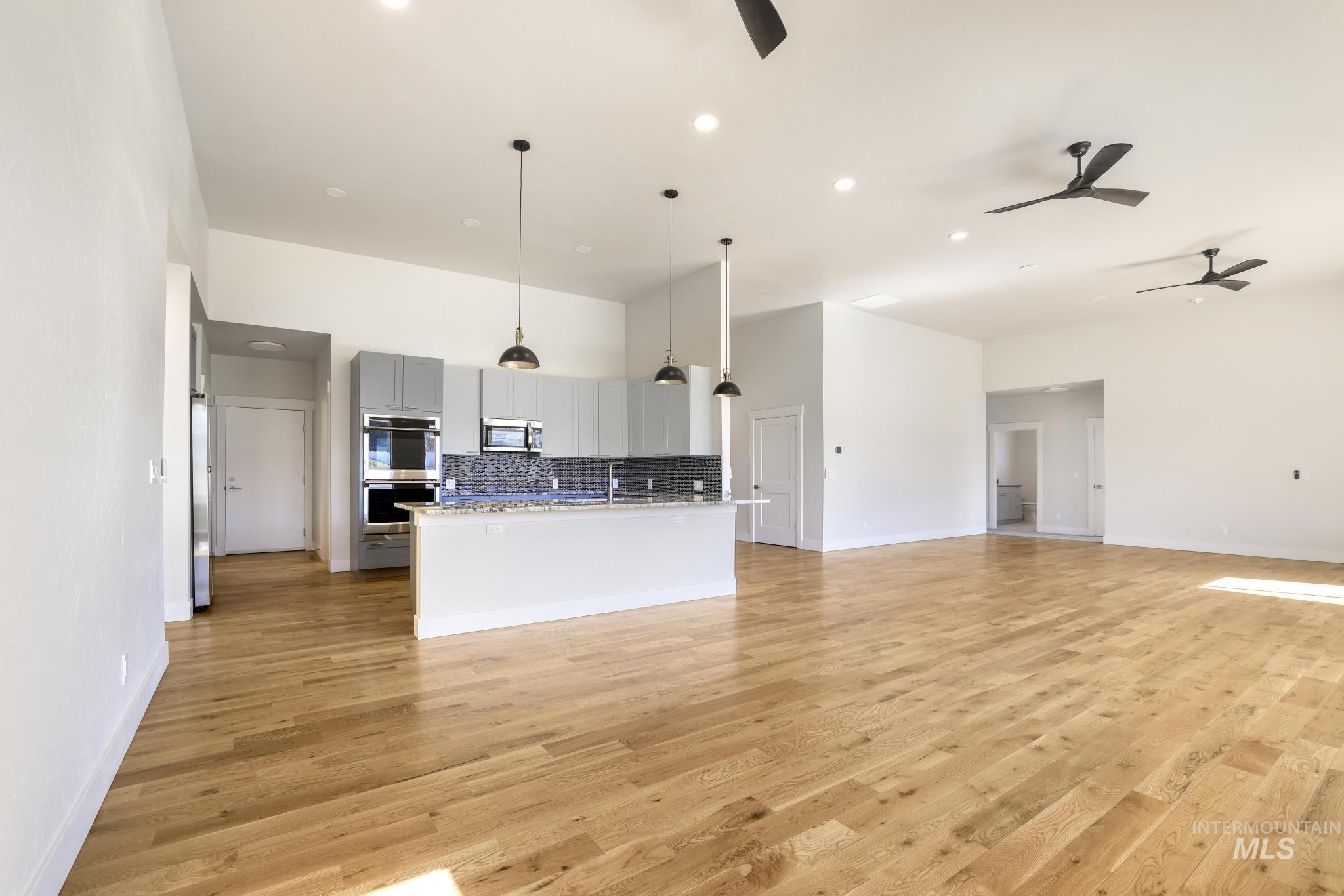 Kitchen with open floor plan, gray cabinetry, a center island with sink, decorative light fixtures, and ceiling fan