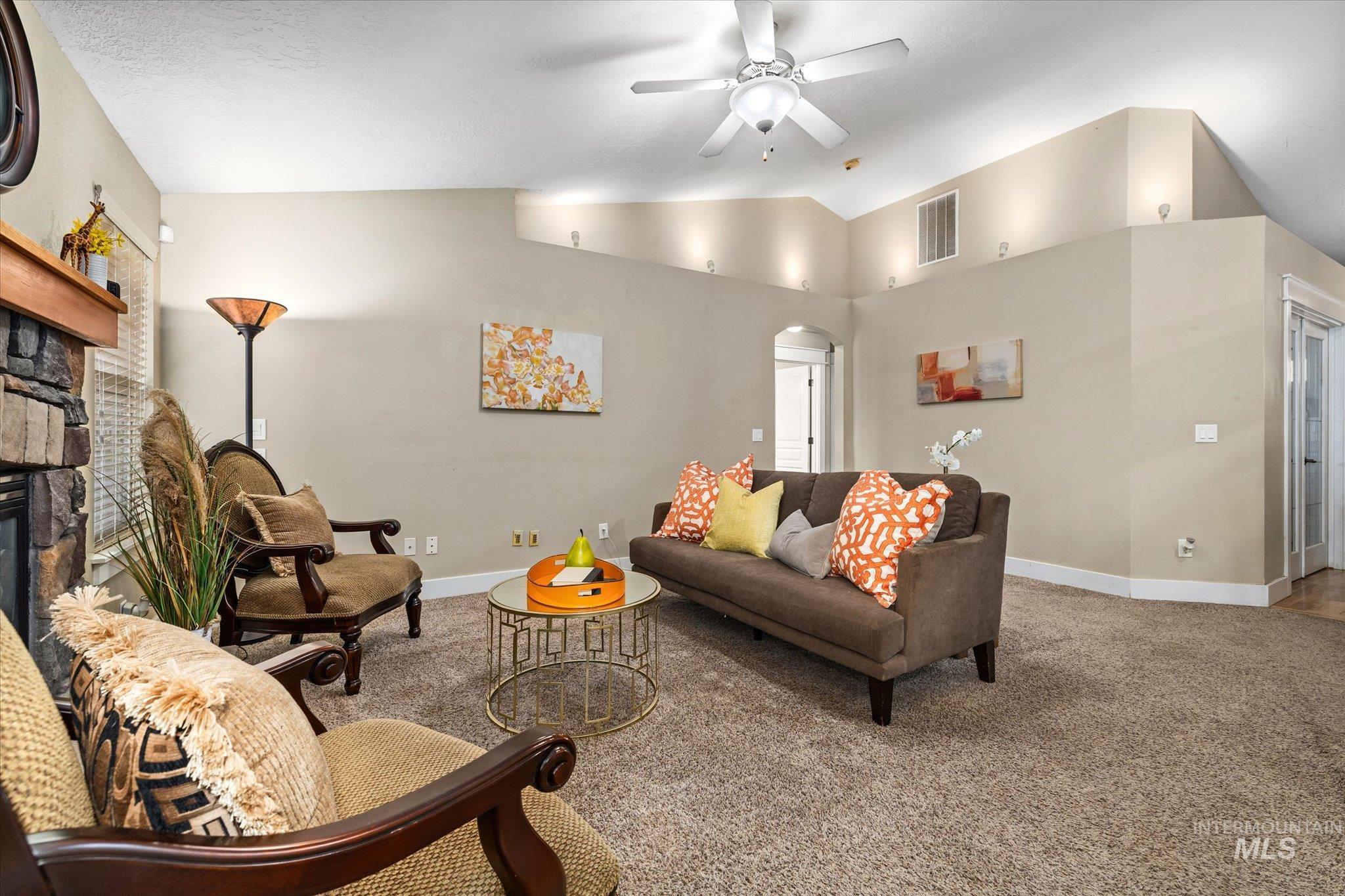 Living room featuring arched walkways, carpet floors, vaulted ceiling, a fireplace, and ceiling fan