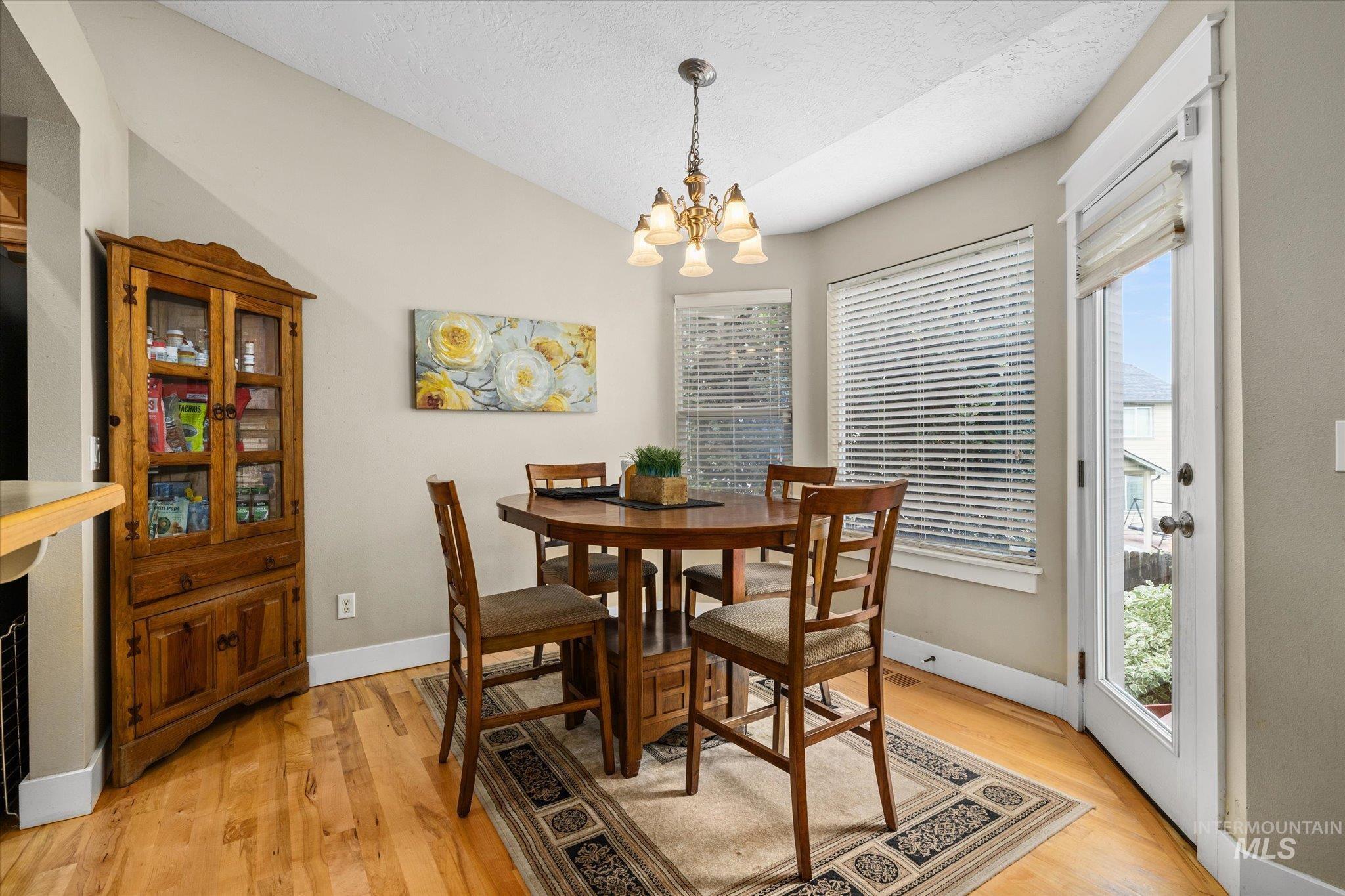 Dining space with light wood-style floors, a chandelier, vaulted ceiling, and a textured ceiling