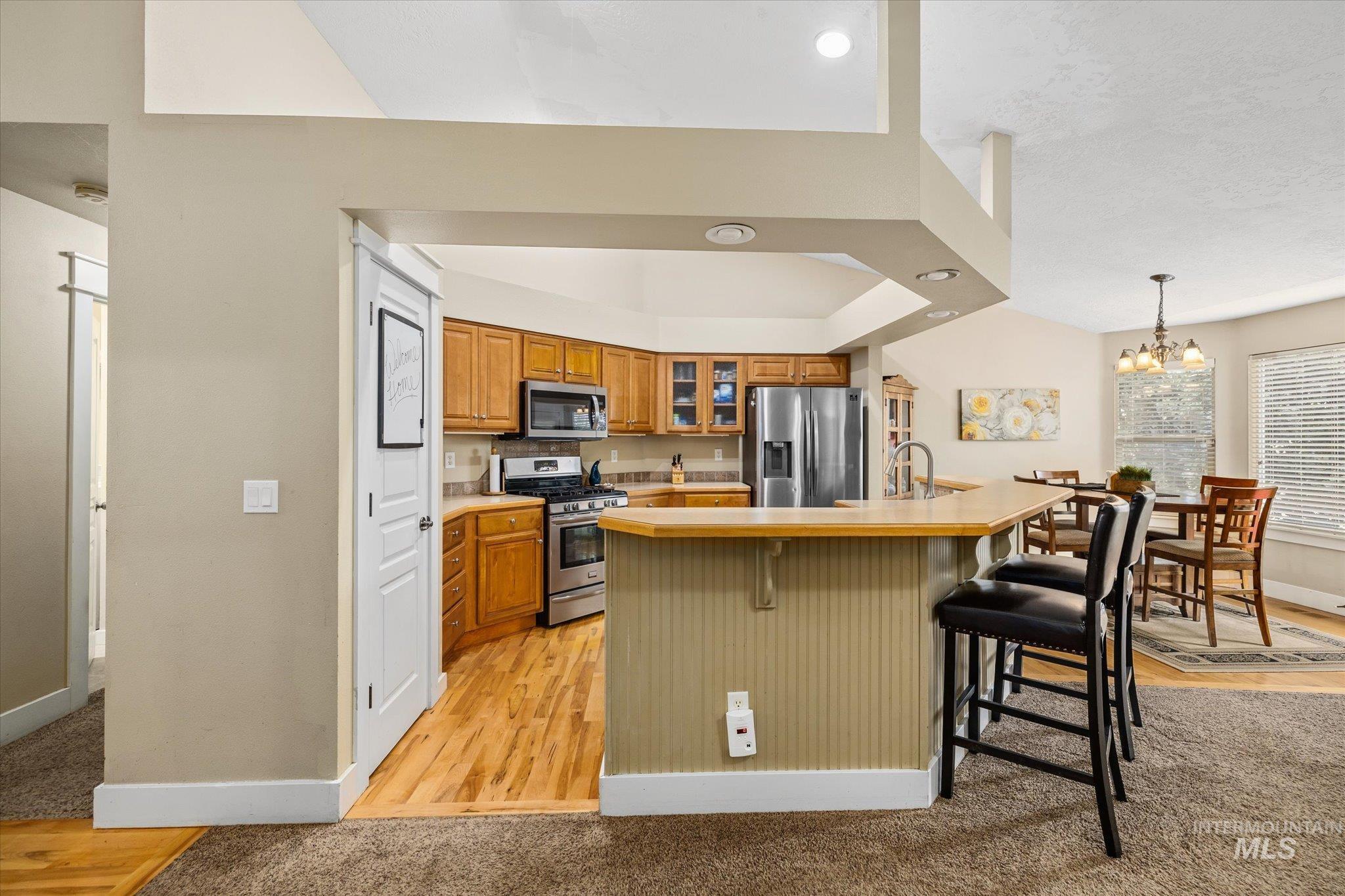 Kitchen featuring hanging light fixtures, a breakfast bar, light countertops, appliances with stainless steel finishes, and glass insert cabinets
