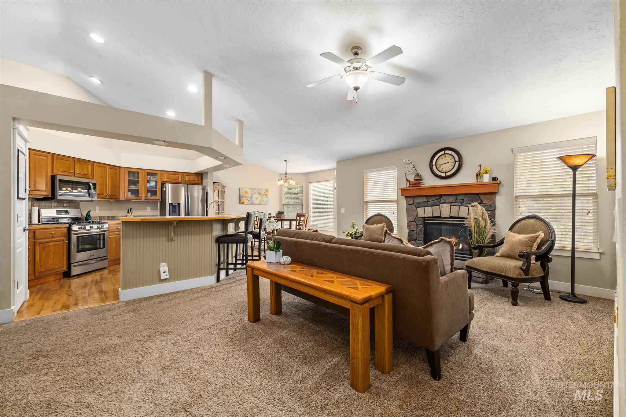 Living room featuring lofted ceiling, light carpet, a fireplace, ceiling fan, and a chandelier