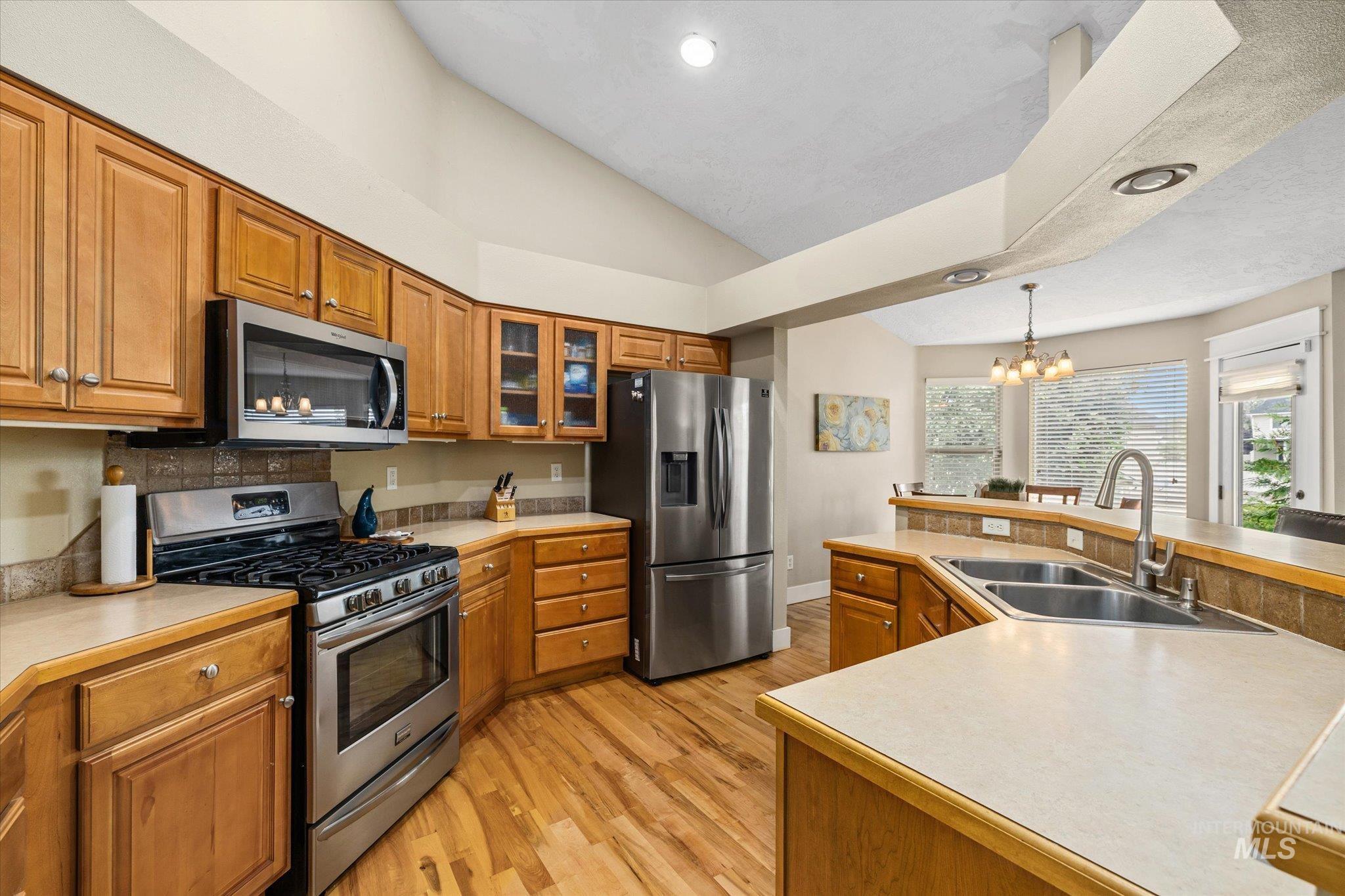 Kitchen with stainless steel appliances, brown cabinets, light wood finished floors, glass insert cabinets, and light countertops