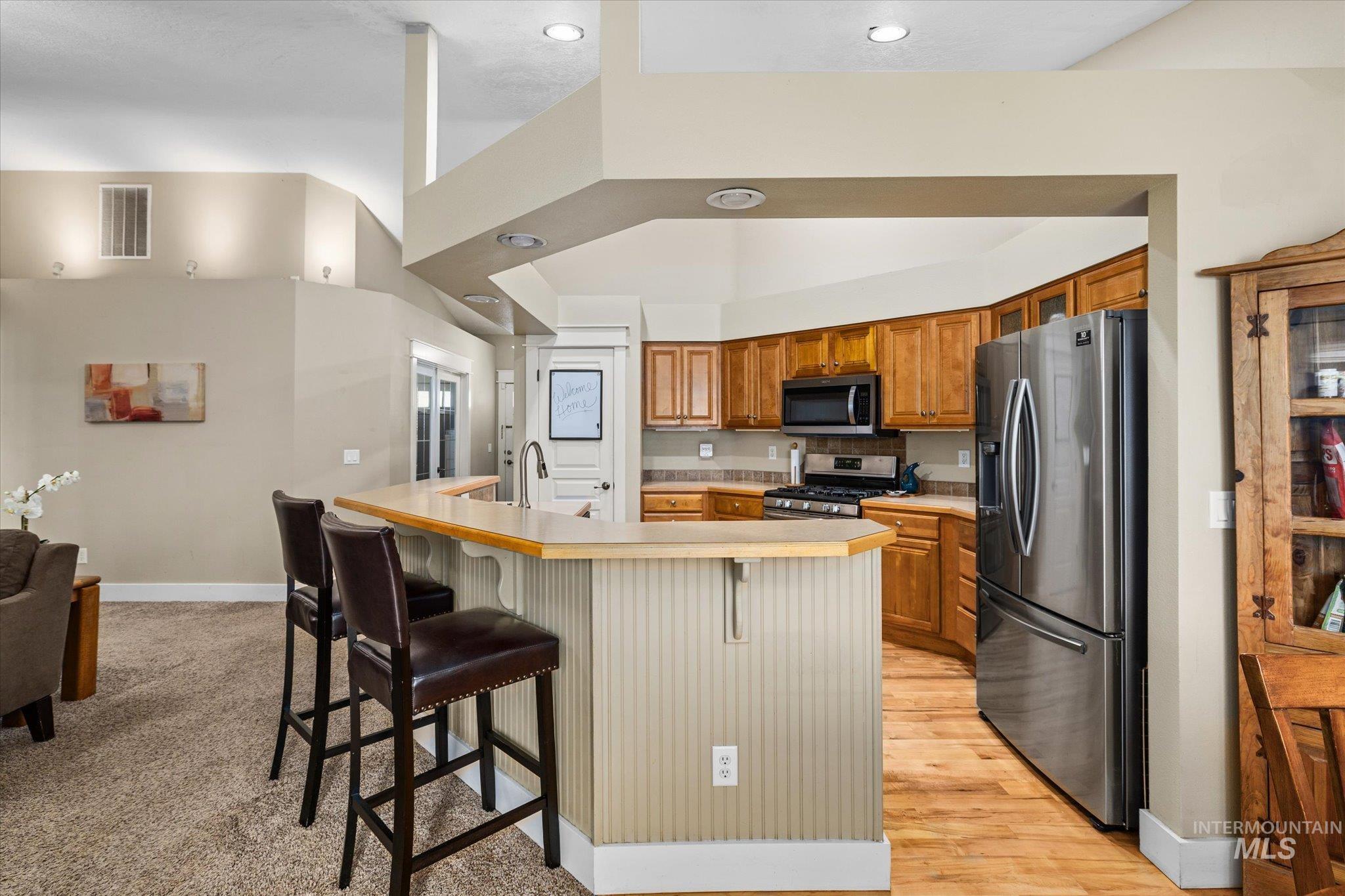 Kitchen featuring light countertops, stainless steel appliances, a breakfast bar area, brown cabinetry, and a kitchen island with sink