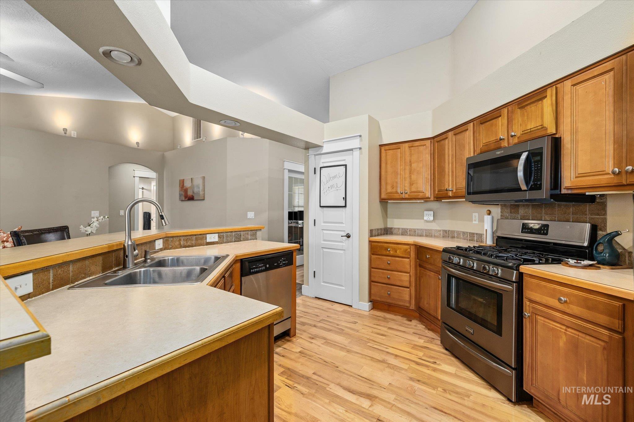 Kitchen with appliances with stainless steel finishes, brown cabinetry, arched walkways, light countertops, and light wood-style floors