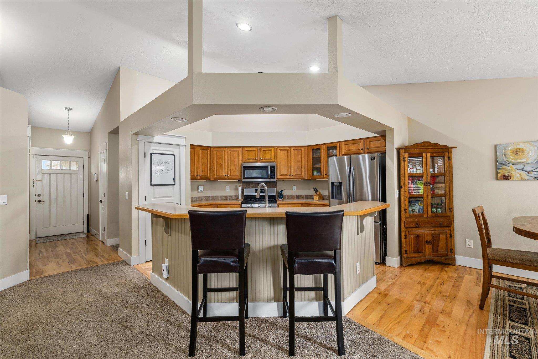 Kitchen featuring light countertops, brown cabinetry, a breakfast bar area, glass insert cabinets, and recessed lighting