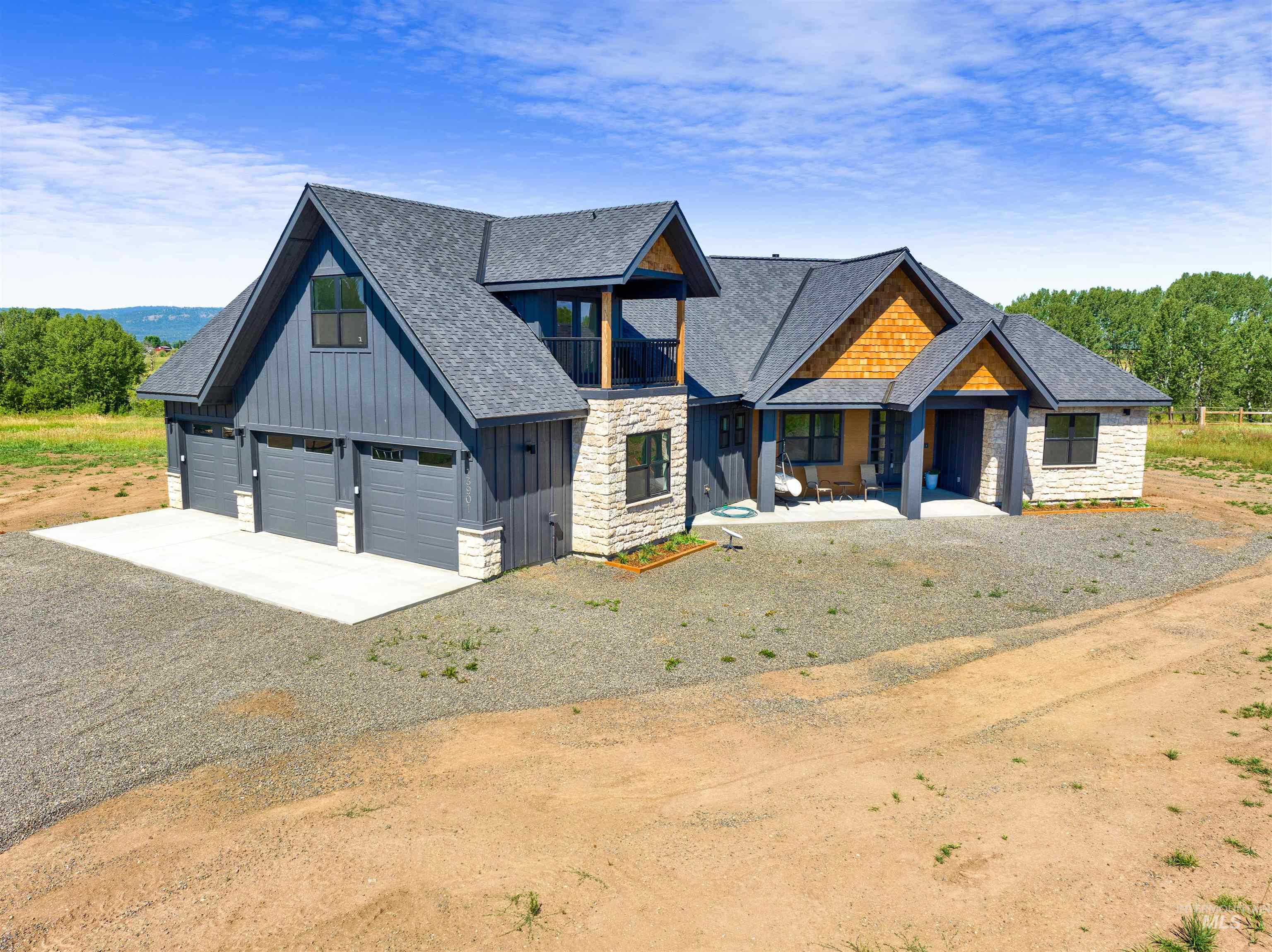 View of front of property featuring gravel driveway, stone siding, board and batten siding, a shingled roof, and a garage