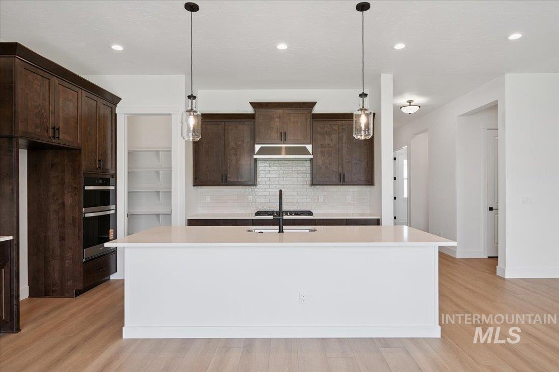 Kitchen with dark brown cabinets, tasteful backsplash, decorative light fixtures, an island with sink, and recessed lighting