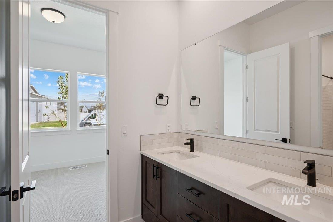 Full bathroom with tasteful backsplash, double vanity, and light colored carpet