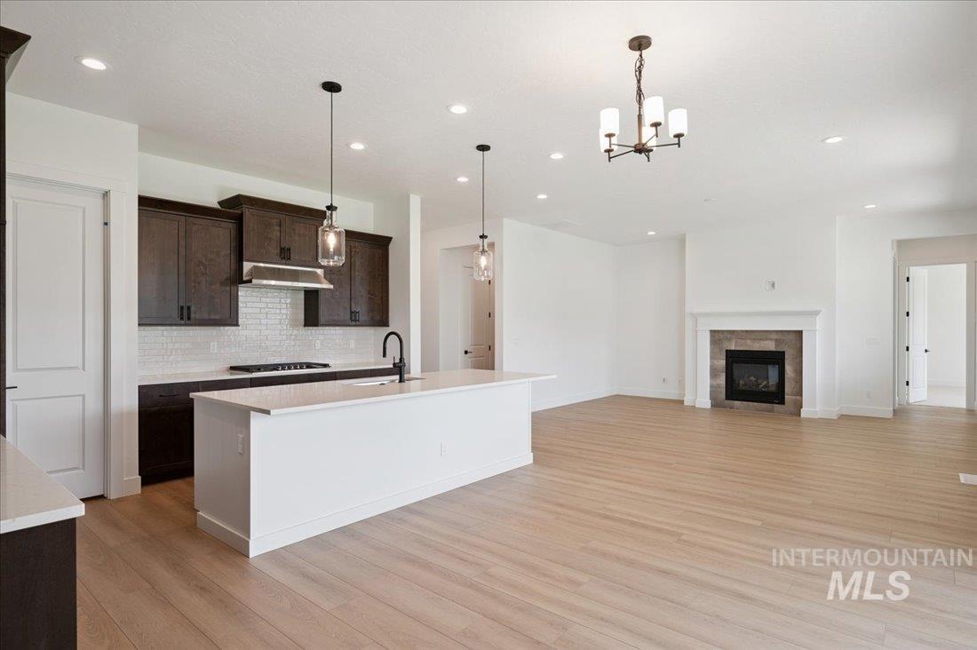 Kitchen featuring dark brown cabinets, pendant lighting, an island with sink, a chandelier, and open floor plan