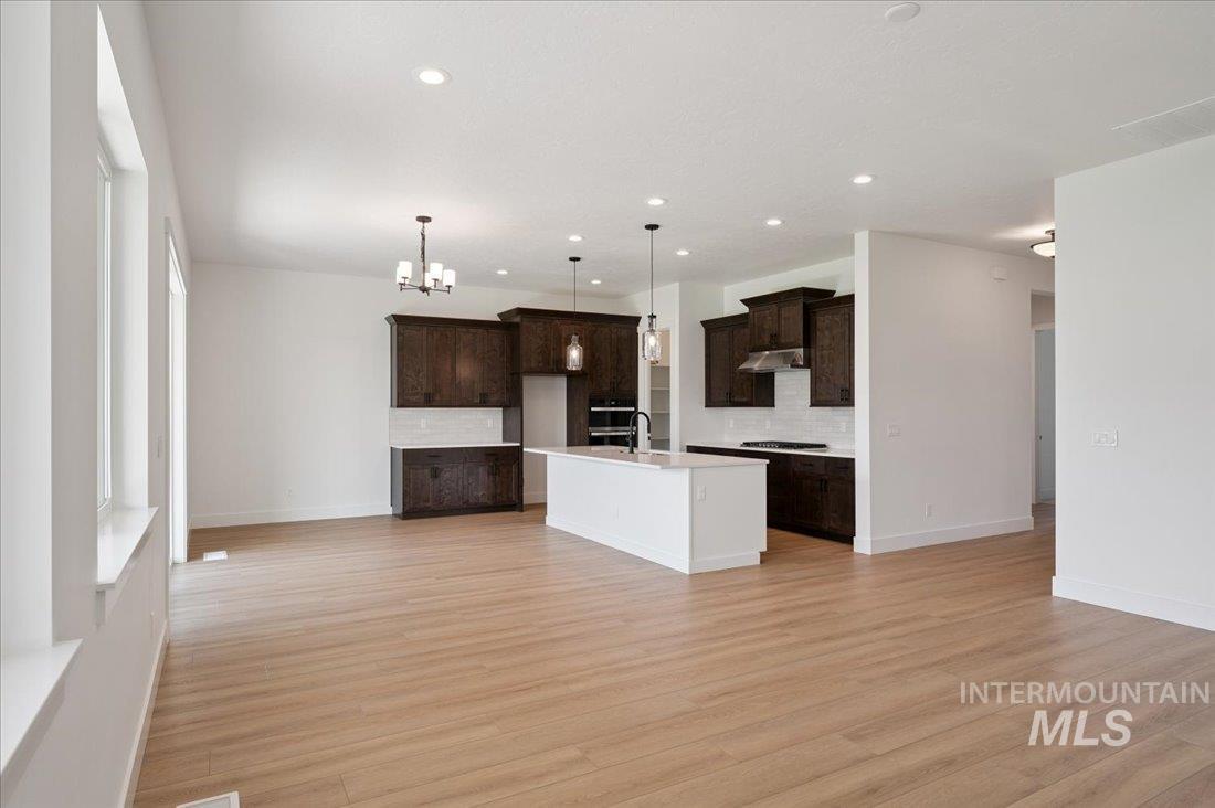 Kitchen with open floor plan, tasteful backsplash, hanging light fixtures, an island with sink, and dark brown cabinetry